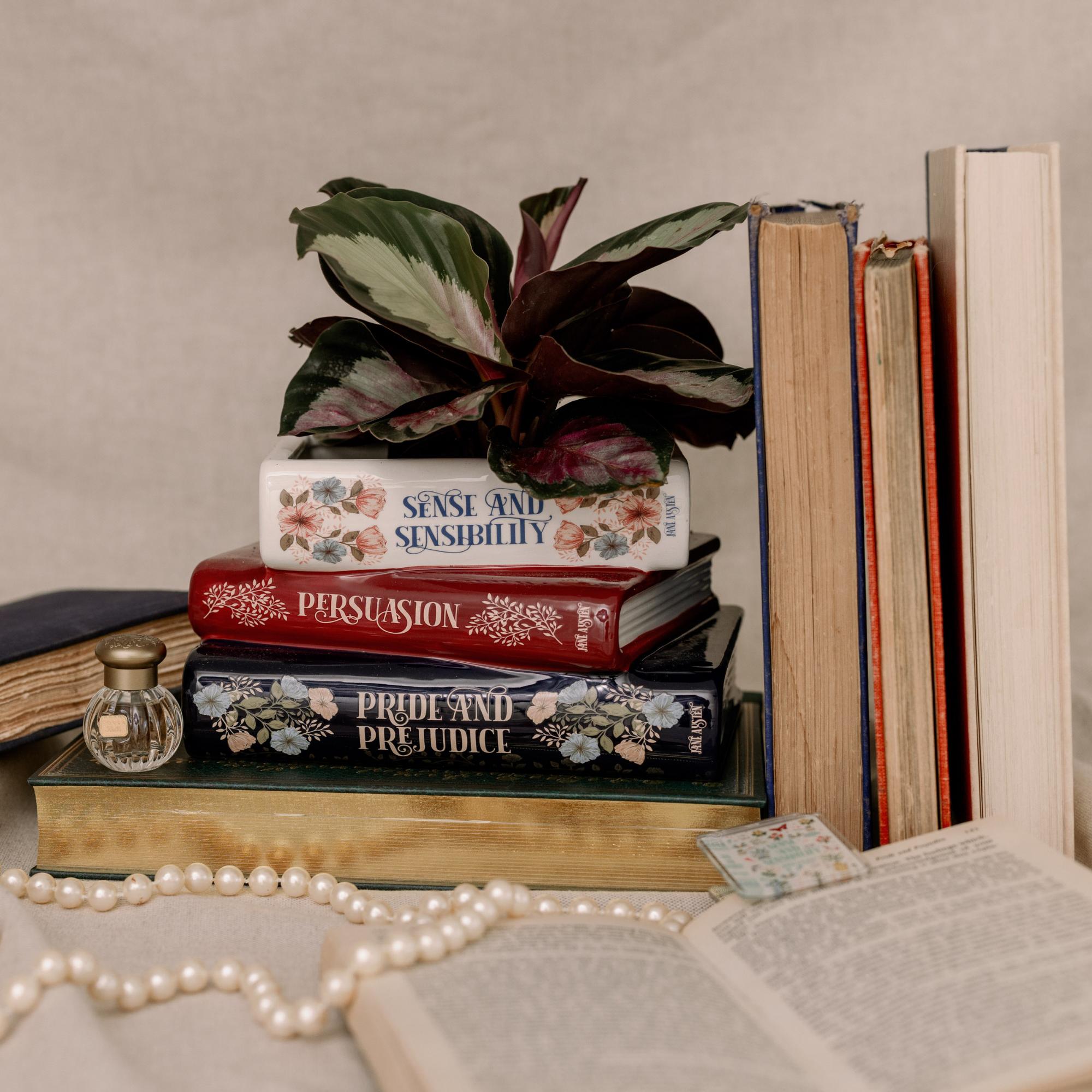Stack of books with decorative covers, a plant, and pearls on a neutral background