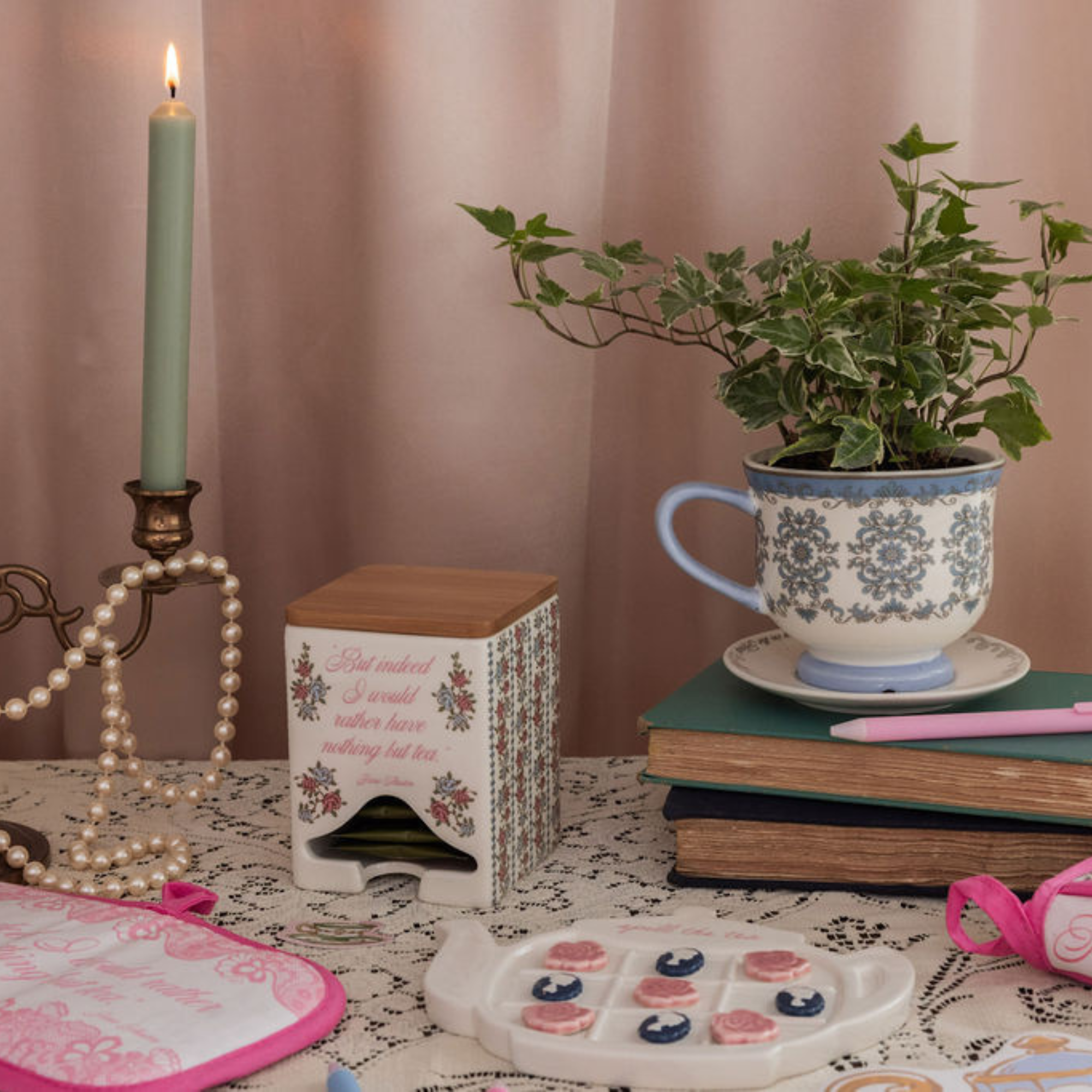 Decorative setting with a teacup, candle, books, and a plant on a table.