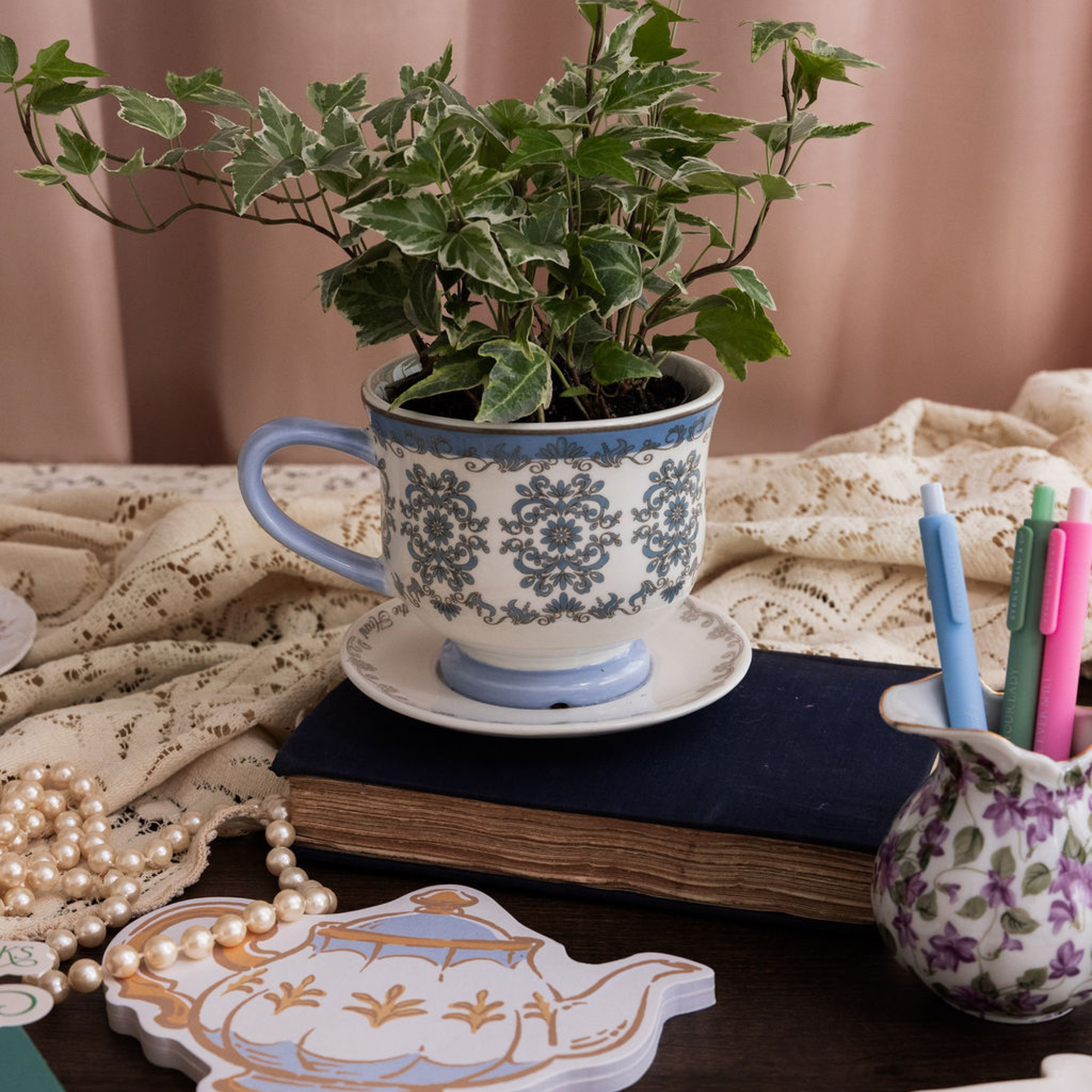 Decorative teacup with plant, notebook, and stationery on a table.