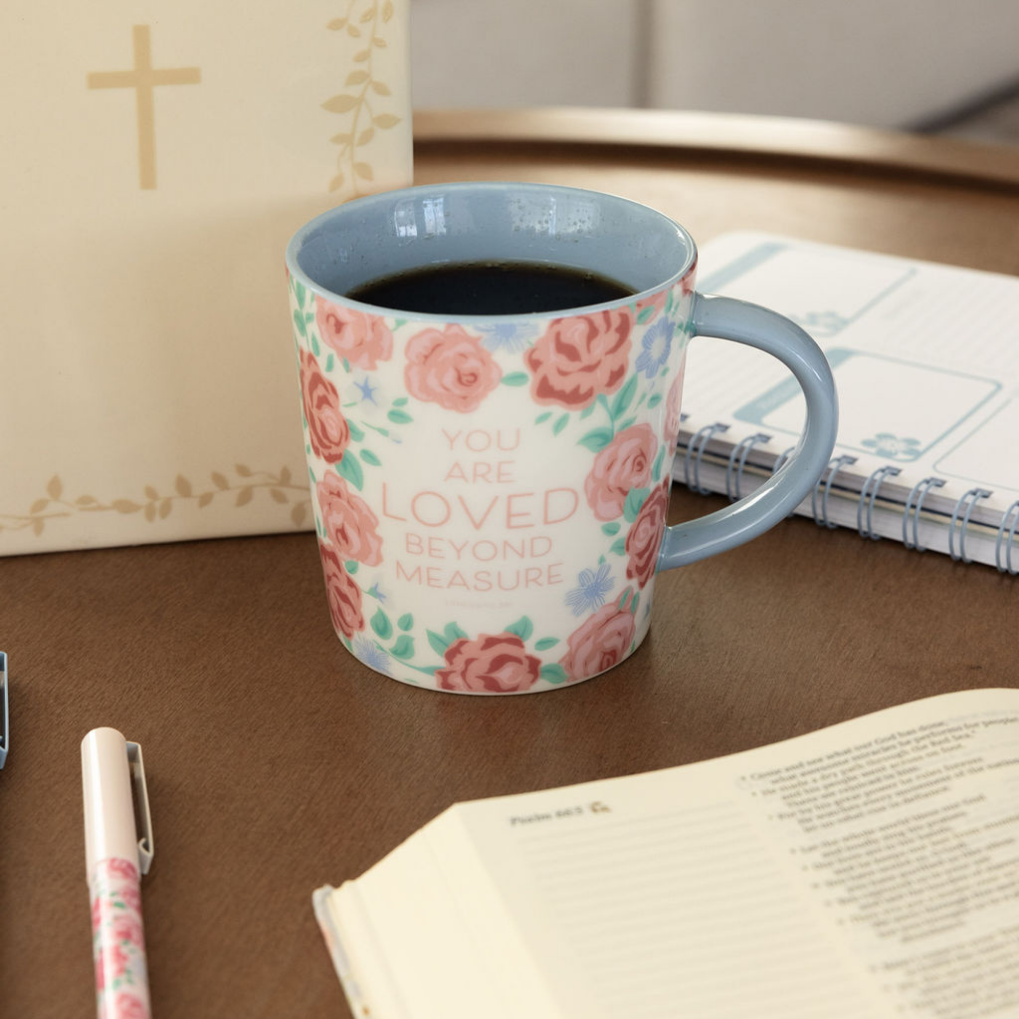 Floral mug with text on a table with books and a pen