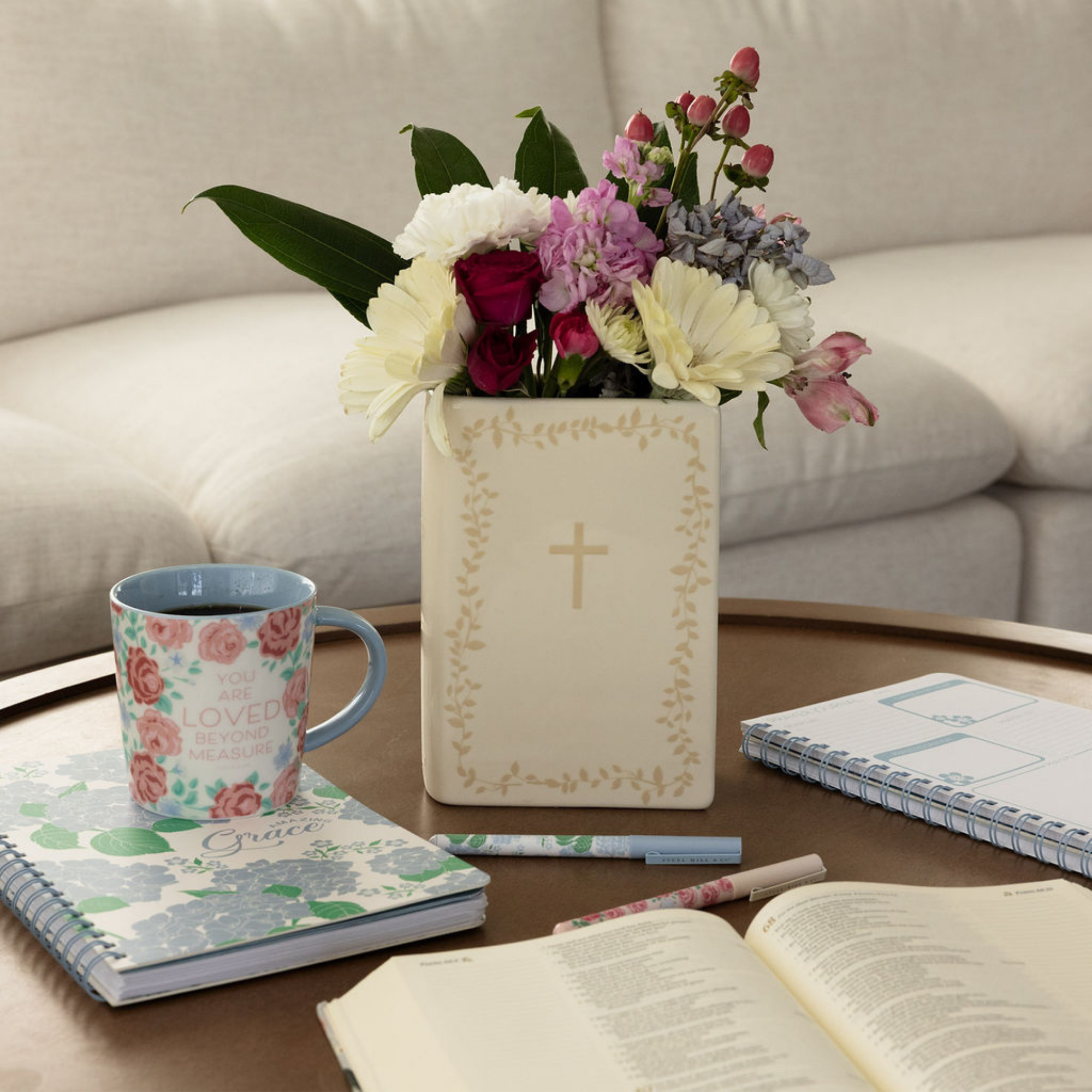 Floral arrangement in a decorative vase on a table with books and a mug.