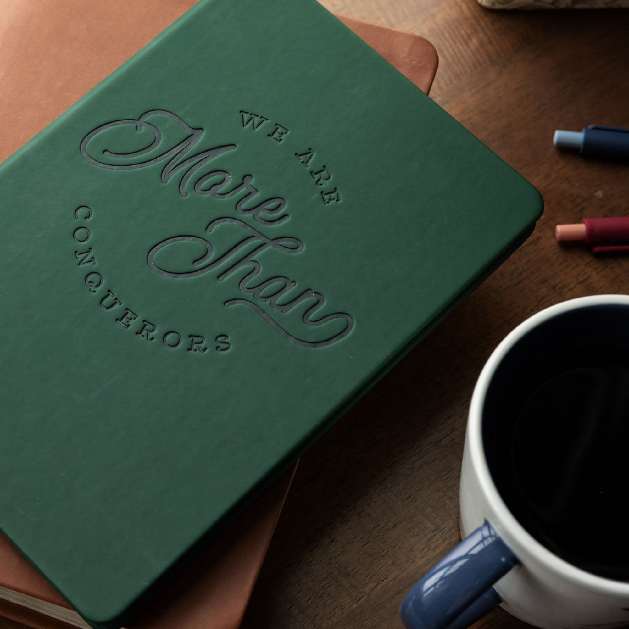 Green notebook with embossed text on a wooden surface next to a cup of coffee.
