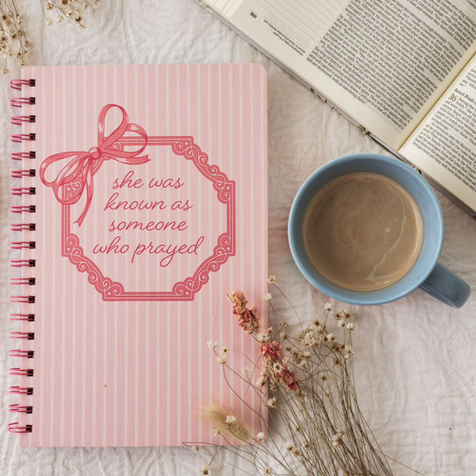 Pink notebook with a motivational quote, blue mug with coffee, and dried flowers on a textured surface.