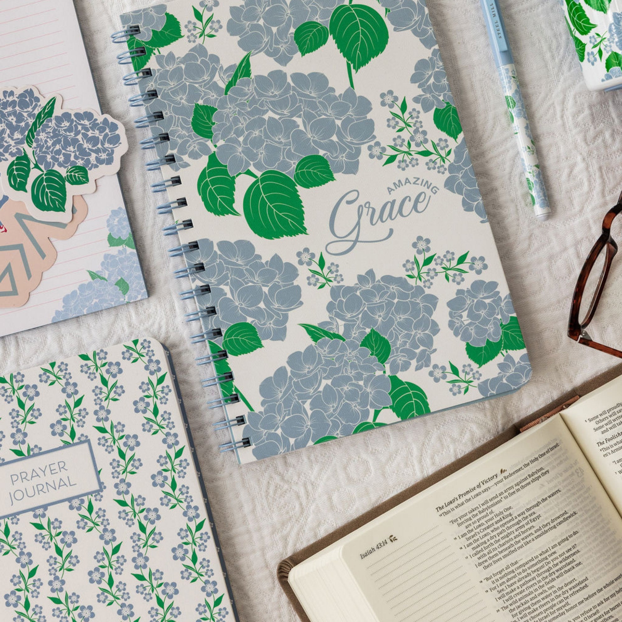 Floral notebook with 'Amazing Grace' text on a textured surface with other notebooks and a pen.