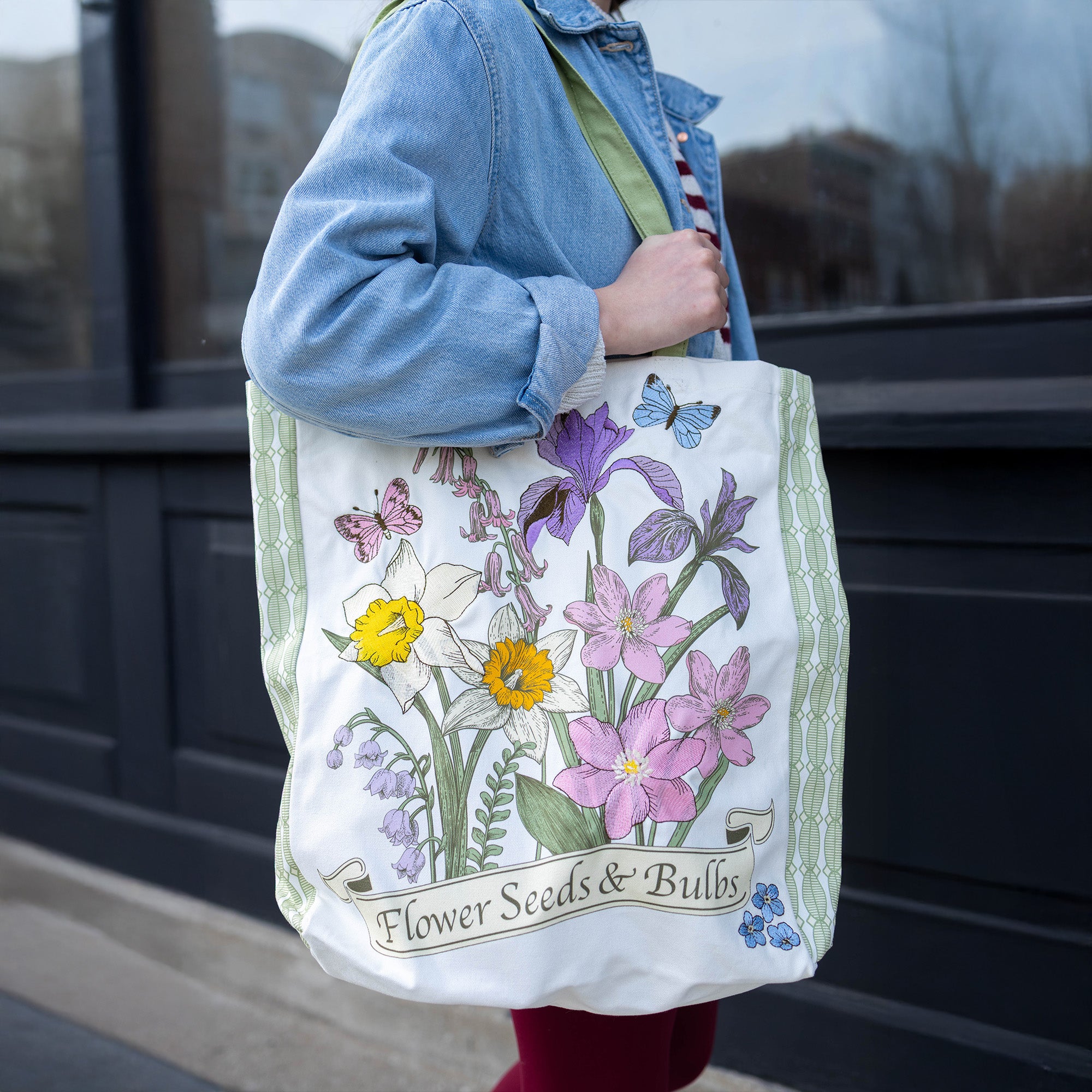 Person holding a tote bag with floral design and text 'Flower Seeds & Bulbs'.
