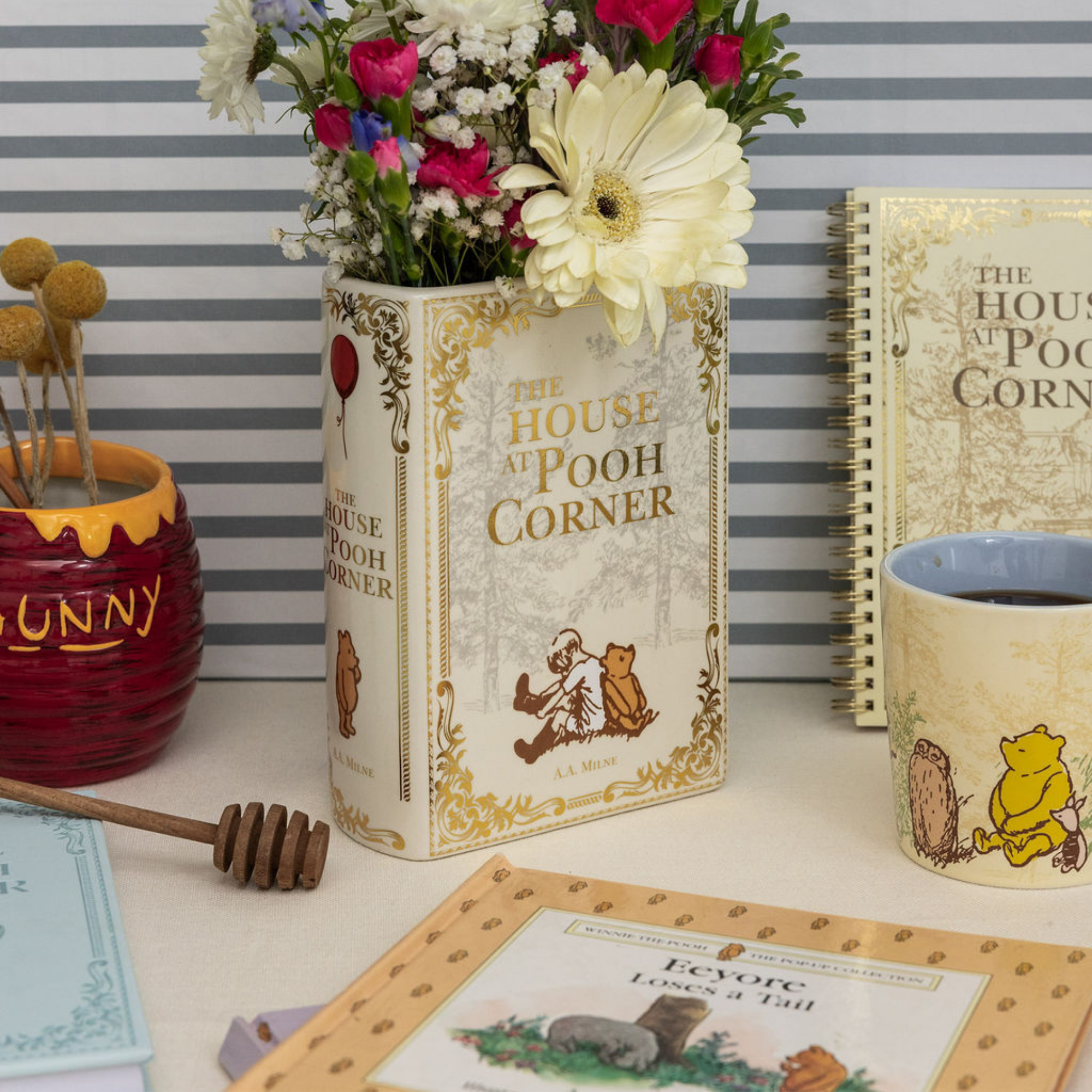 Decorative items including a book-shaped vase with flowers, a mug, and a honey pot on a striped background.