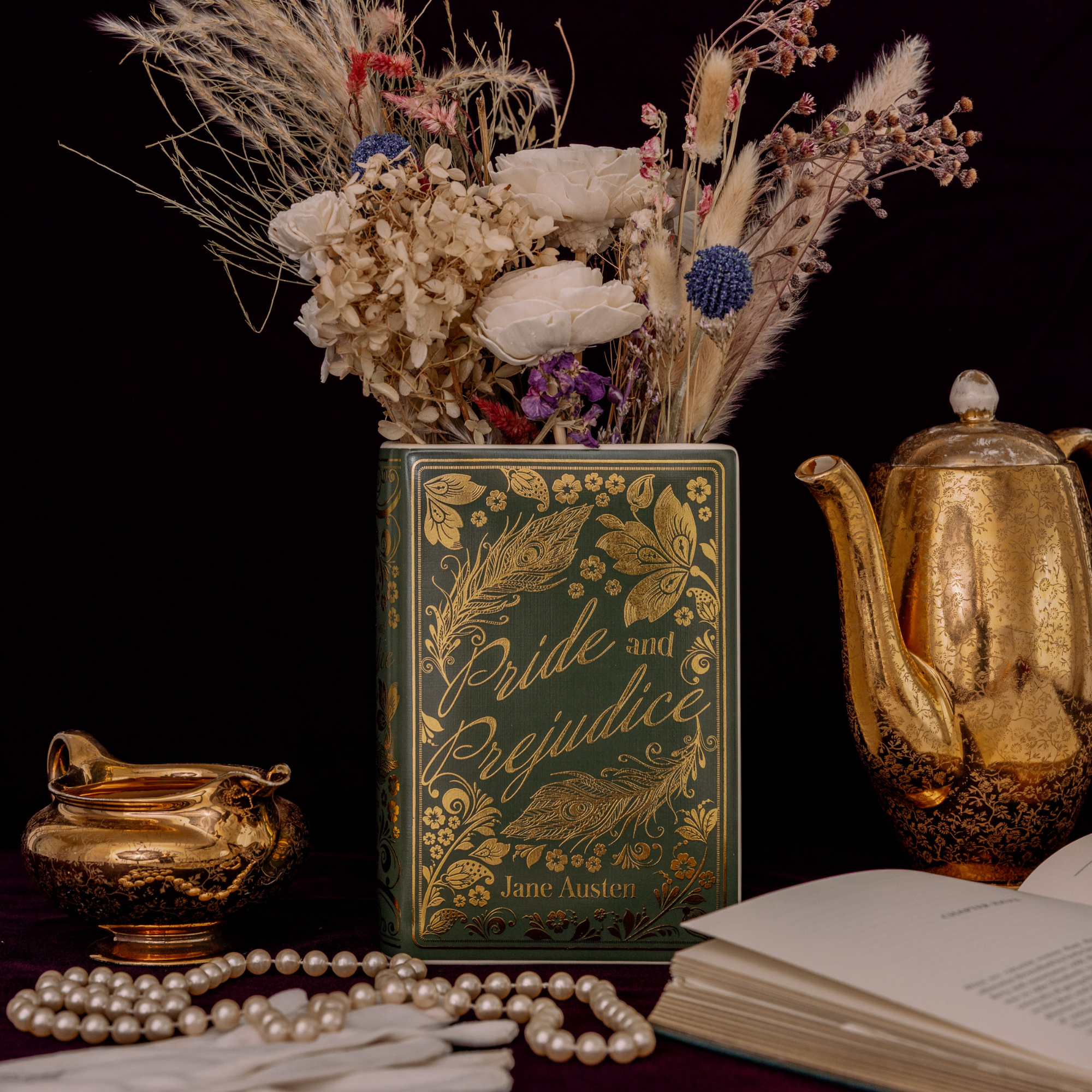Decorative vase with dried flowers, 'Pride and Prejudice' book, pearls, and a teapot on a dark background