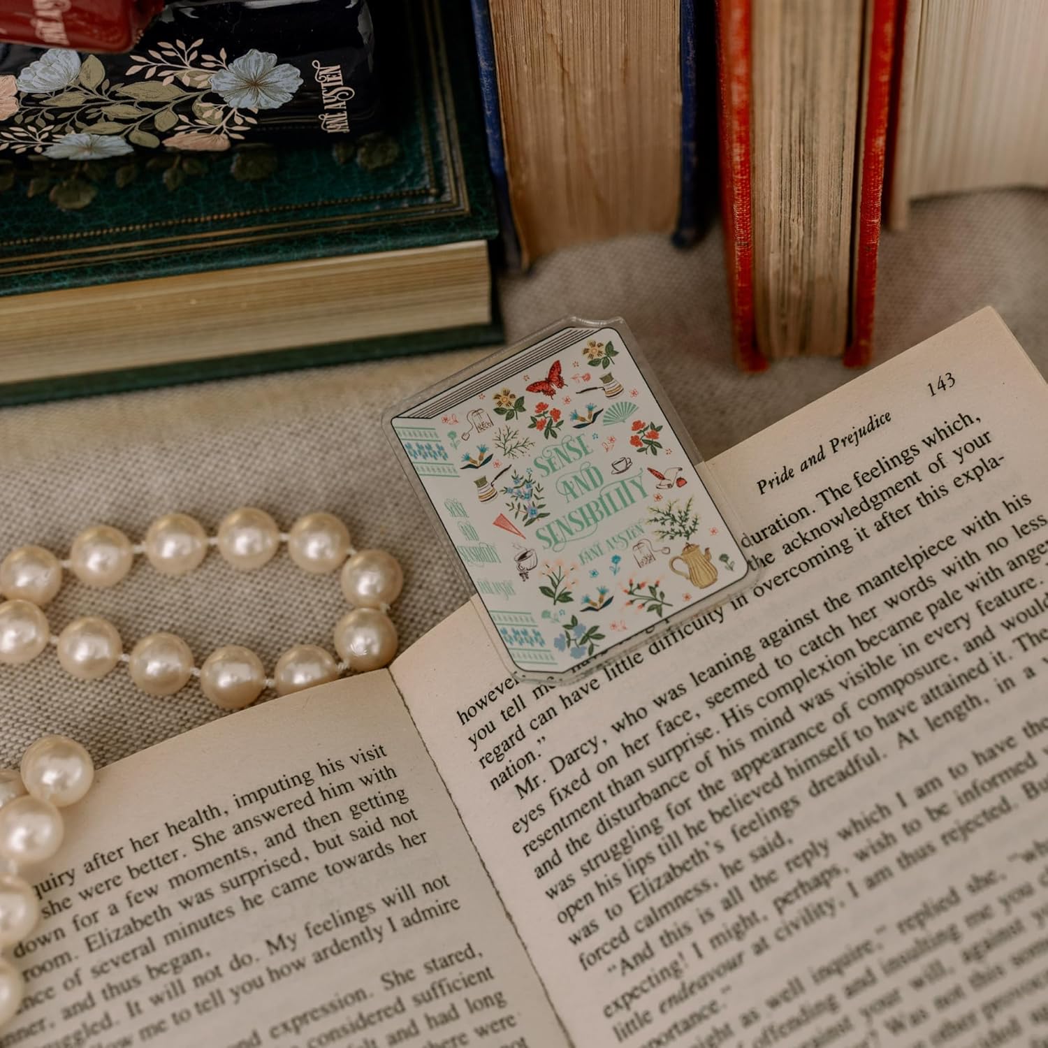 Open book with a decorative card and pearl necklace on a textured surface