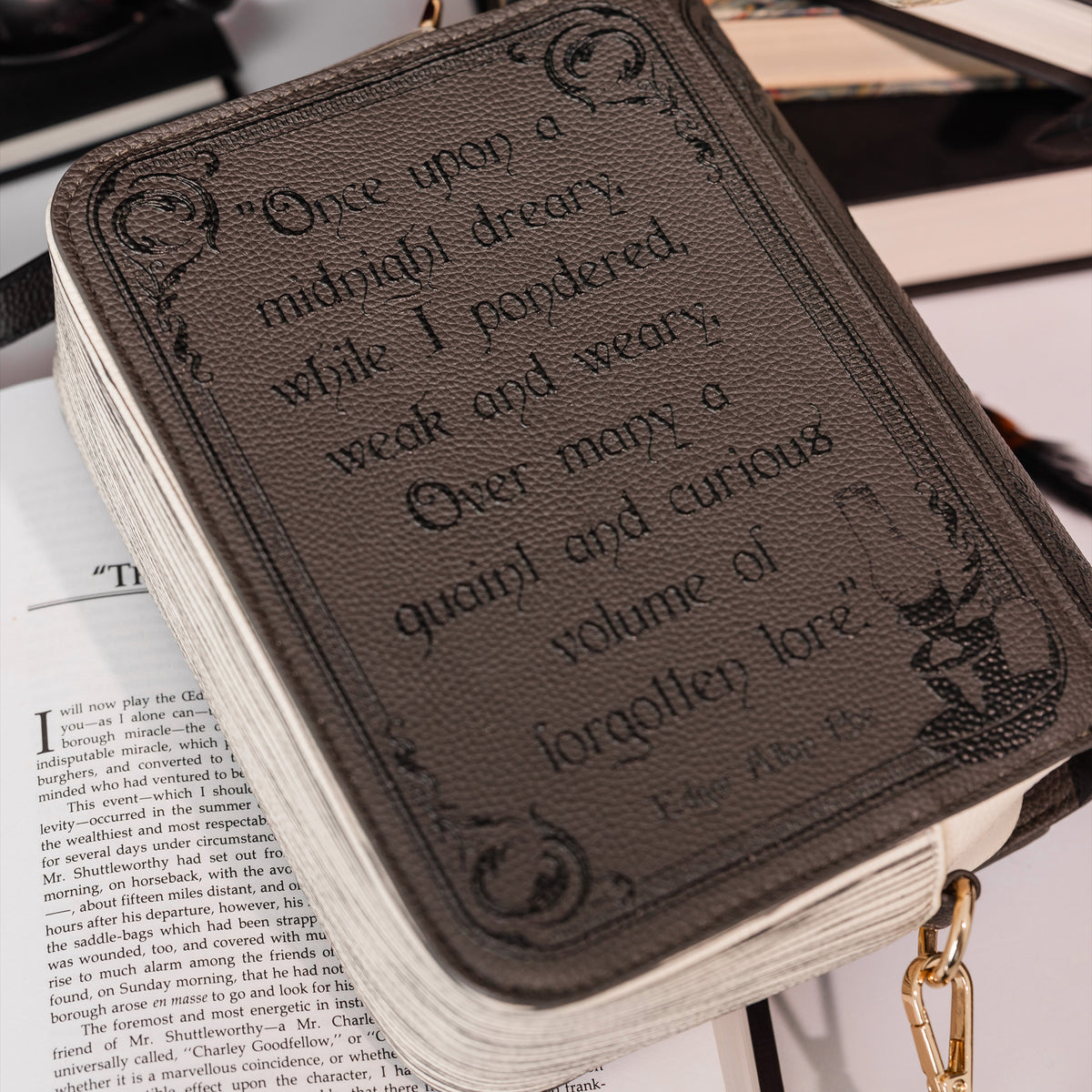 A close-up of a brown faux-leather book bag with gothic-style printed text on the front, resting on an open book with a gold-tone ring pull visible on the right.