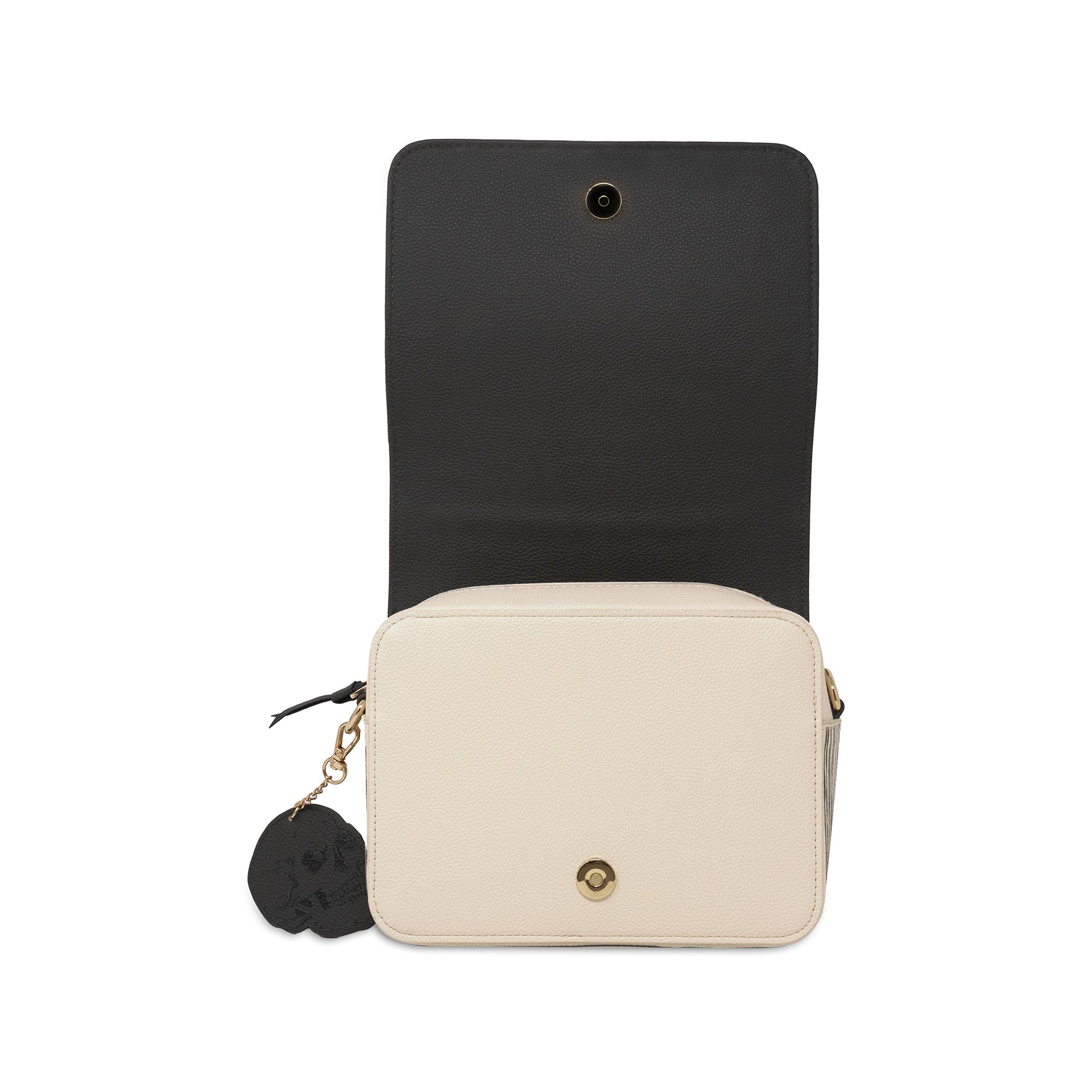 A structured crossbody bag shown open, featuring a cream-colored front flap with a gold snap button and a black interior flap with a gold eyelet. A black skull-shaped charm hangs from a gold zipper pull on the left side, all set against a plain white background.