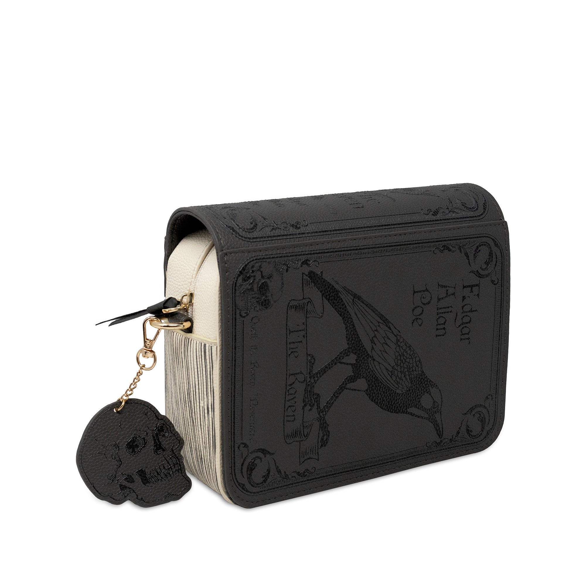 A black faux-leather book-style crossbody featuring embossed gothic artwork of a raven with a cream-colored page edge visible on the left and a dangling black skull charm on a gold chain.