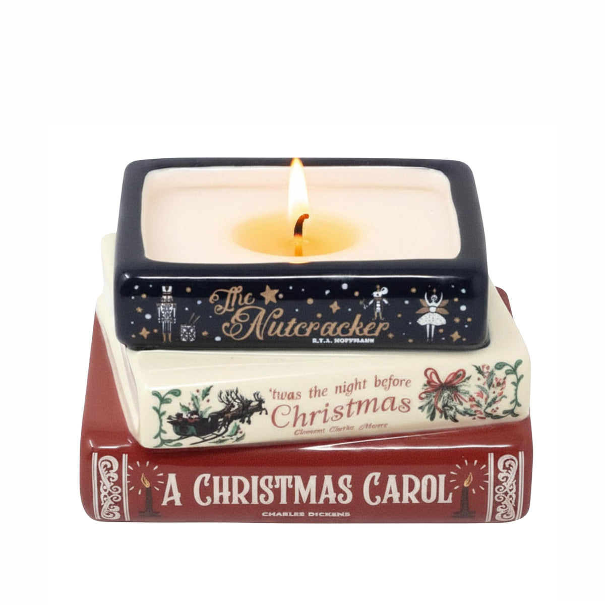 A square ceramic candle holder styled like a stack of Christmas books, with a lit candle inside. The top book is dark navy blue with gold Nutcracker illustrations and text; the middle book is cream with red and green holiday text and illustrations; the bottom book is dark red with white text reading 'A Christmas Carol.'