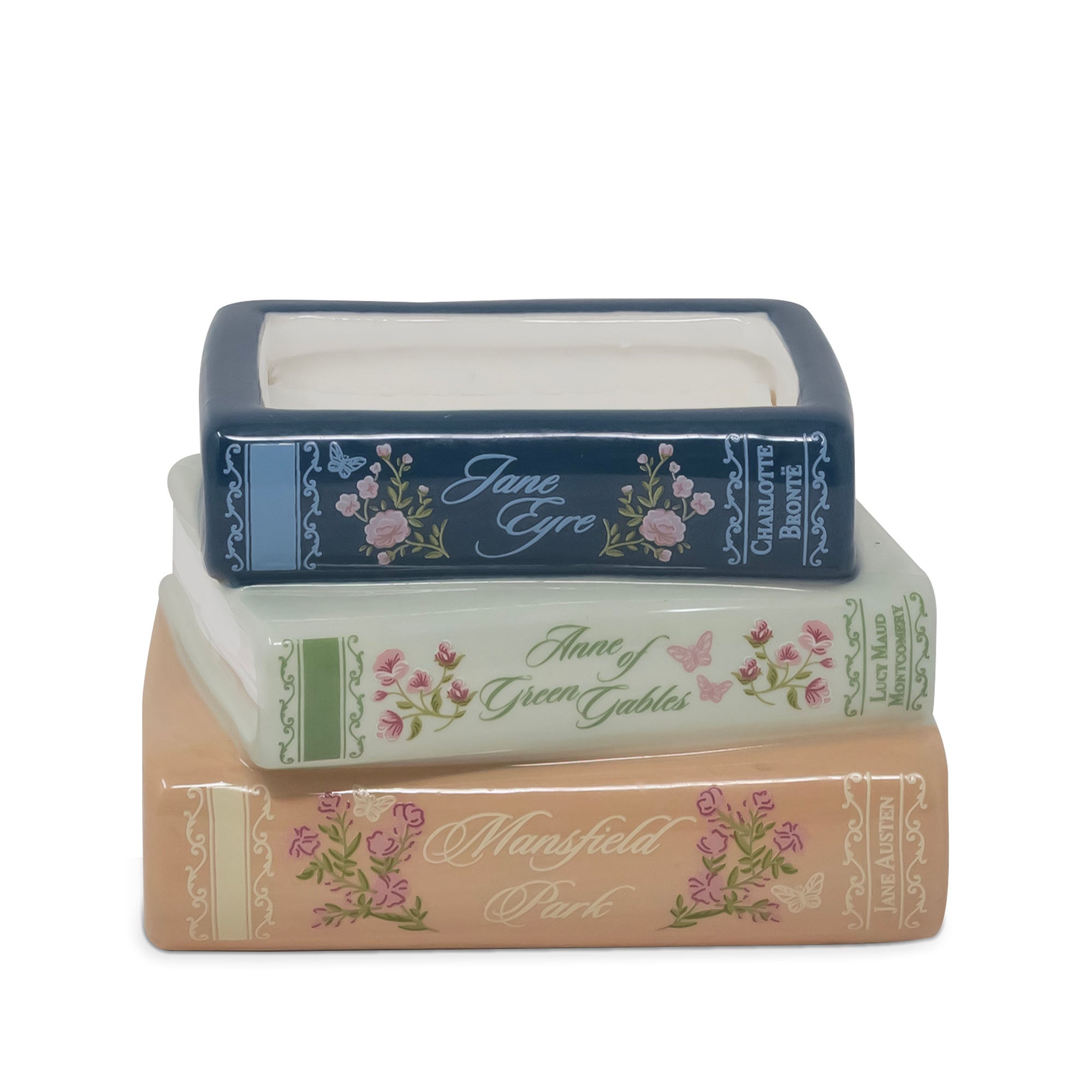 Three stacked book-shaped decorative candle with floral designs and titles including Jane Eyre, Anne of Green Gables, and Mansfield Park, on a white background.