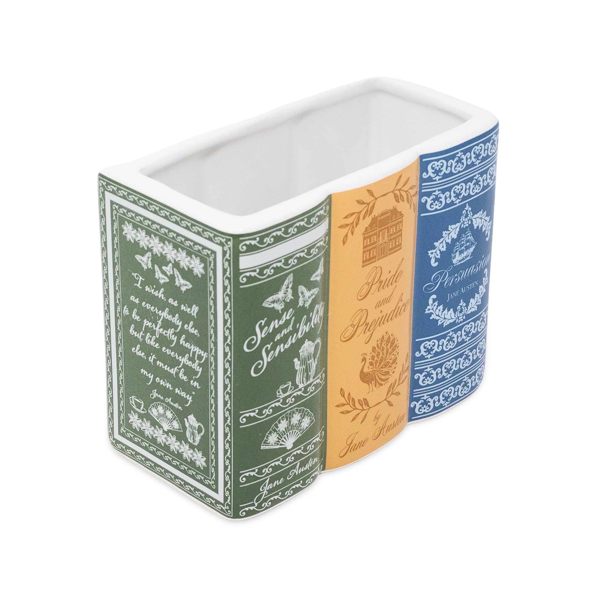 A rectangular ceramic planter or container with a three-spine book design. The left spine is dark green with white script and botanical illustrations, the middle spine is tan with gold script and a house illustration, and the right spine is blue with white decorative patterns.
