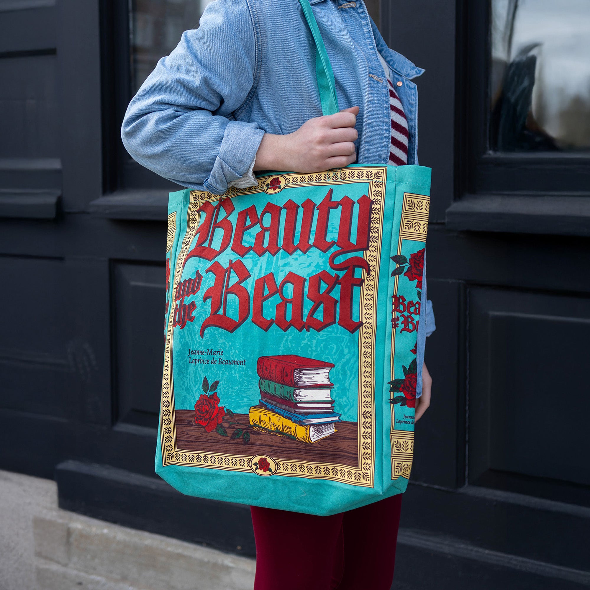 Person holding a 'Beauty and the Beast' themed tote bag in front of a dark door.