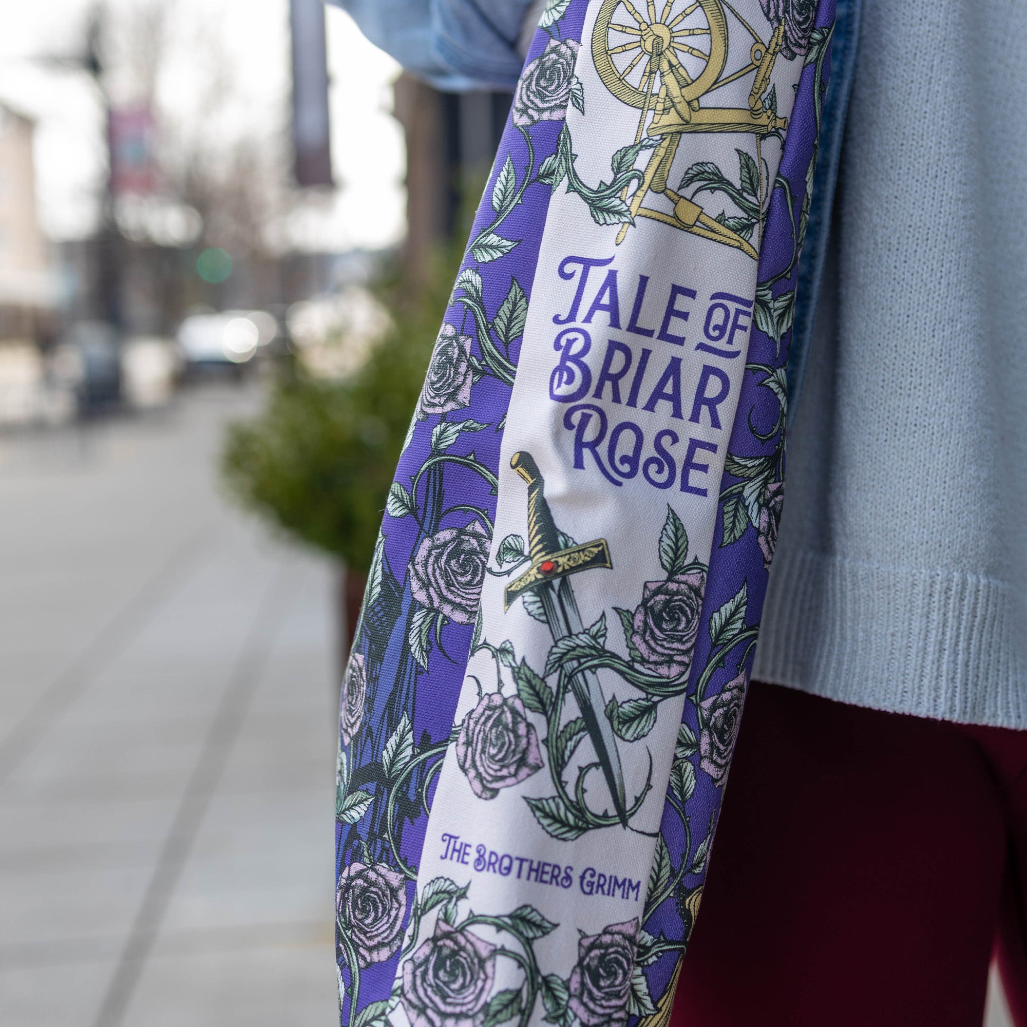 Tote bag with 'Tale of Briar Rose' design and 'The Brothers Grimm' text, worn by a person on a blurred street background.