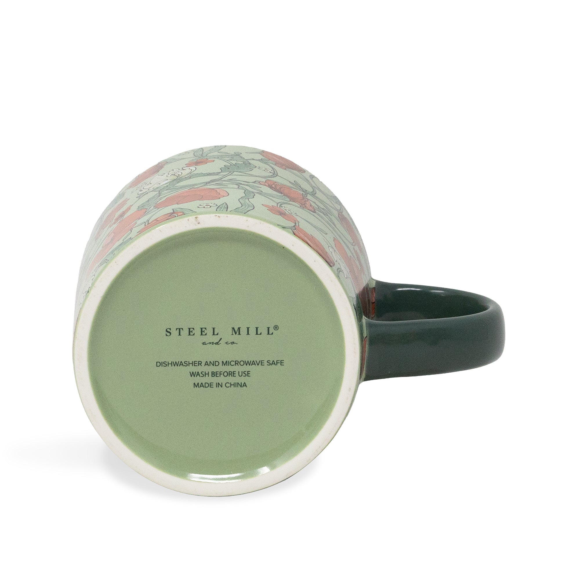 A ceramic mug shown from a side angle, displaying its dark green handle, a light green interior base printed with 'STEEL MILL and co', and a pink and green floral patterned exterior.