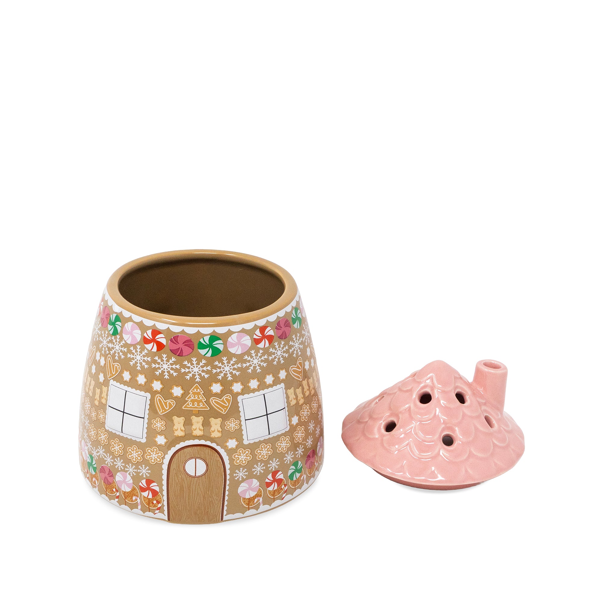 A ceramic gingerbread house-shaped vase with a pink lid, shown on a plain white background. The candle holder features a tan base decorated with white snowflakes and colorful holiday motifs like gingerbread men, candy canes, and hearts.
