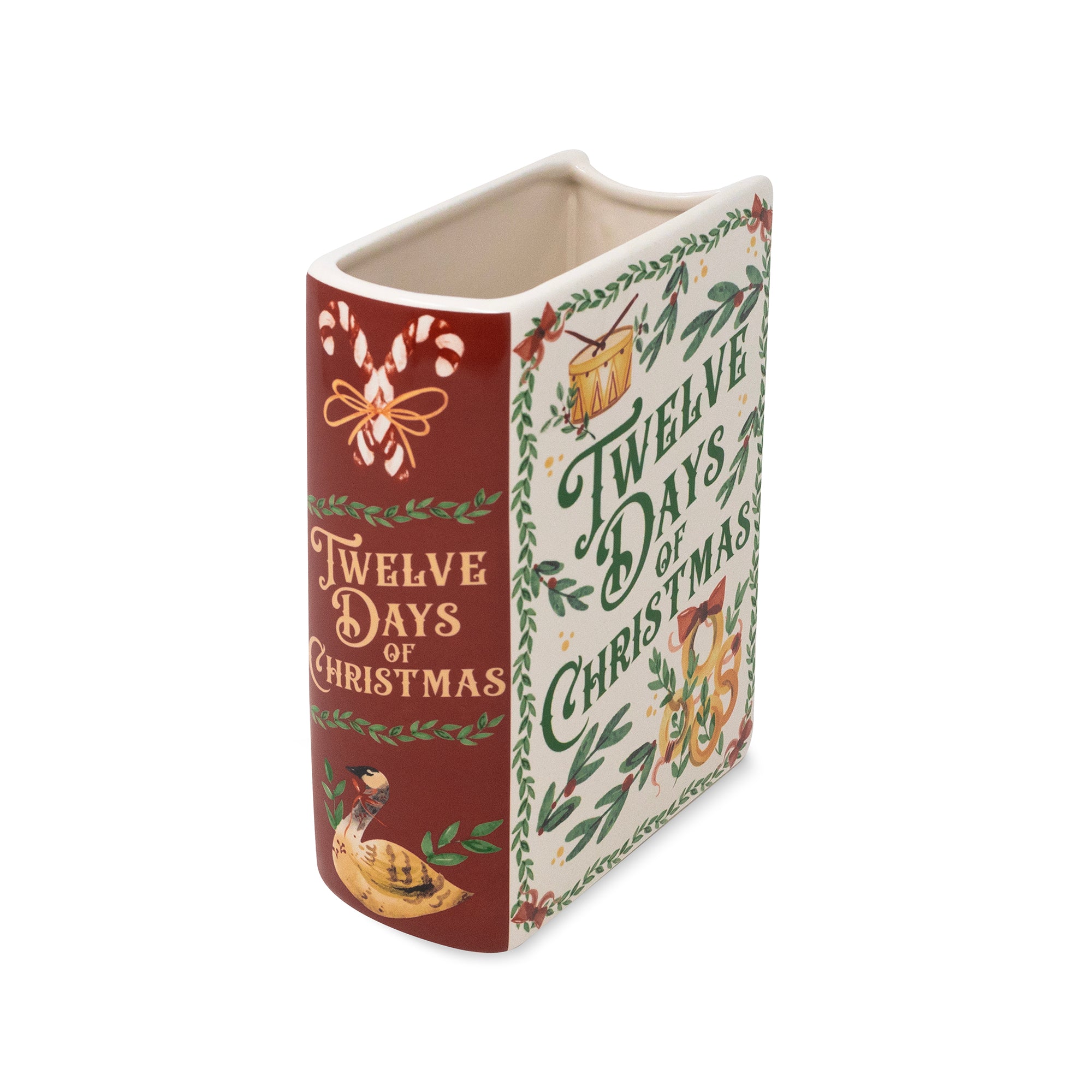 A ceramic Christmas book-shaped container with a dark red spine and cream pages, decorated with illustrations of a candy cane, a duck, and green holly leaves and text reading 'Twelve Days of Christmas'.