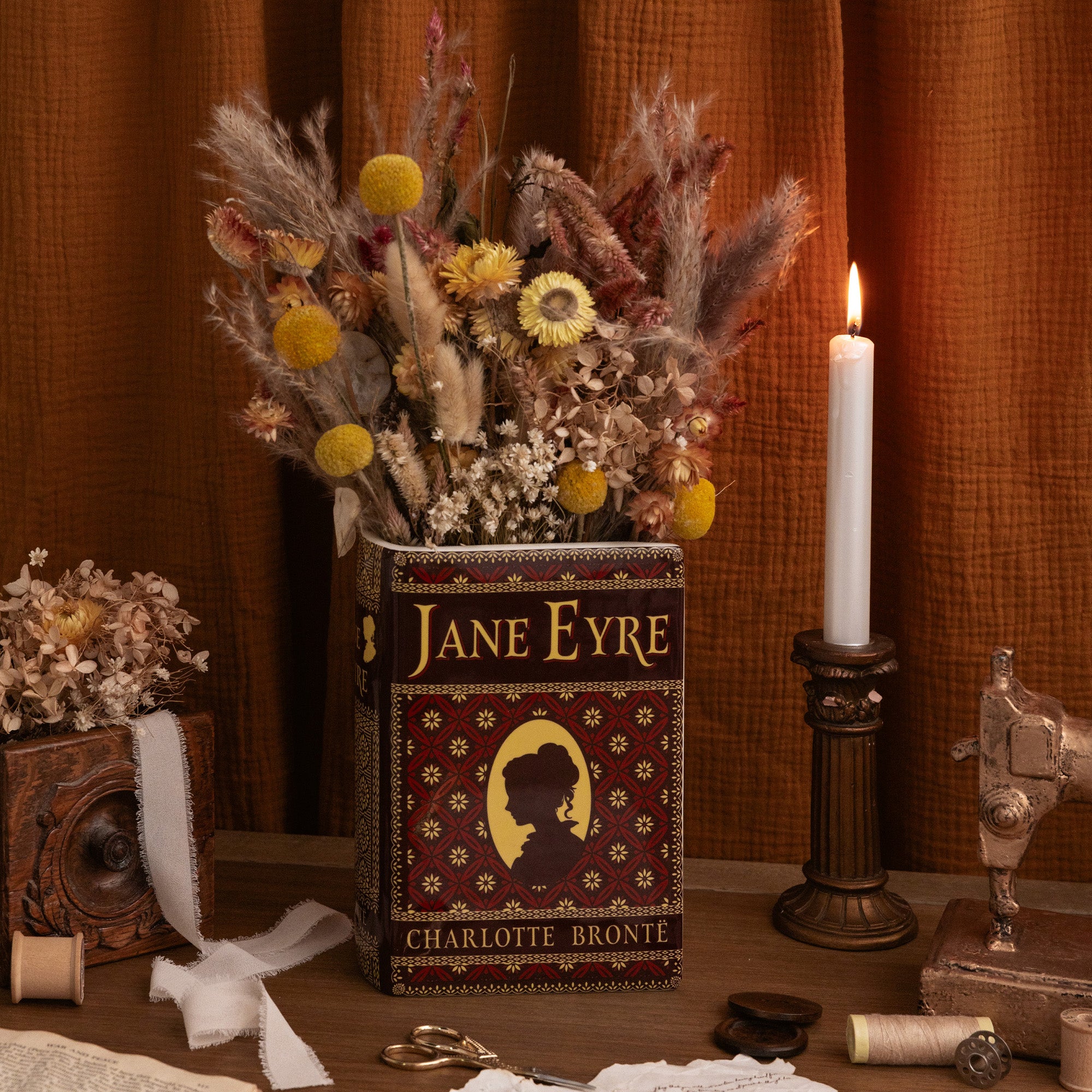 A decorative book-shaped vase featuring Jane Eyre cover art, shown on a plain white background. The design includes a dark brown and black background with ornate gold patterns, the title 'Jane Eyre' on the spine and front, and a gold silhouette portrait.