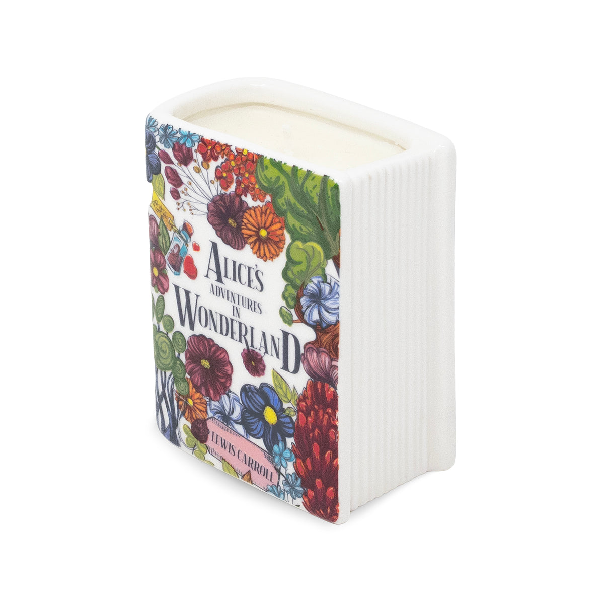 A square white candle vessel with a ribbed side and a colorful illustrated front panel featuring flowers and the text 'Alice's Adventures Wonderland'