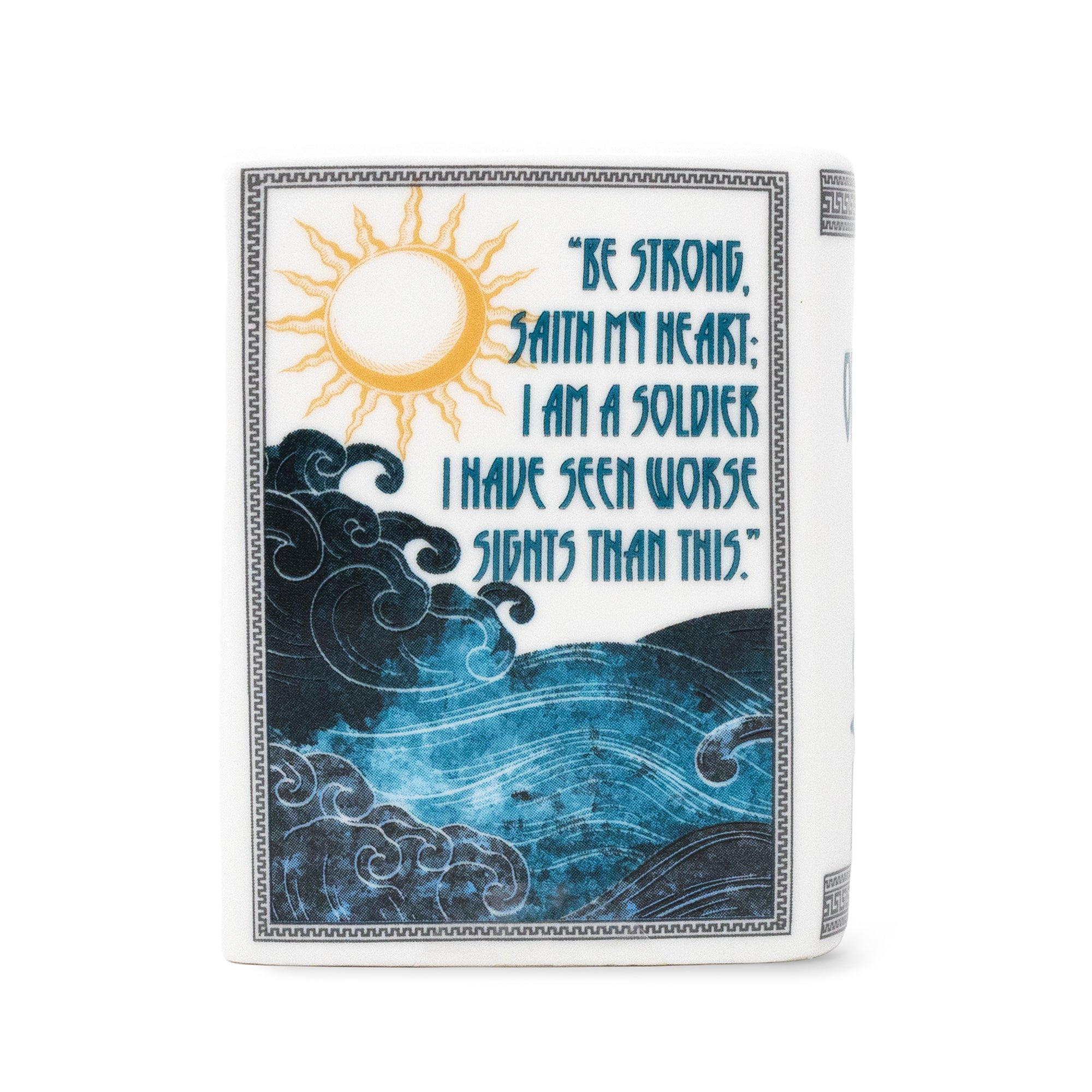 A white candle with a printed cover design featuring a yellow sun, blue ocean waves, and a quote that reads, 'BE STRONG, SAITH MY HEART. I AM A SOLDIER.