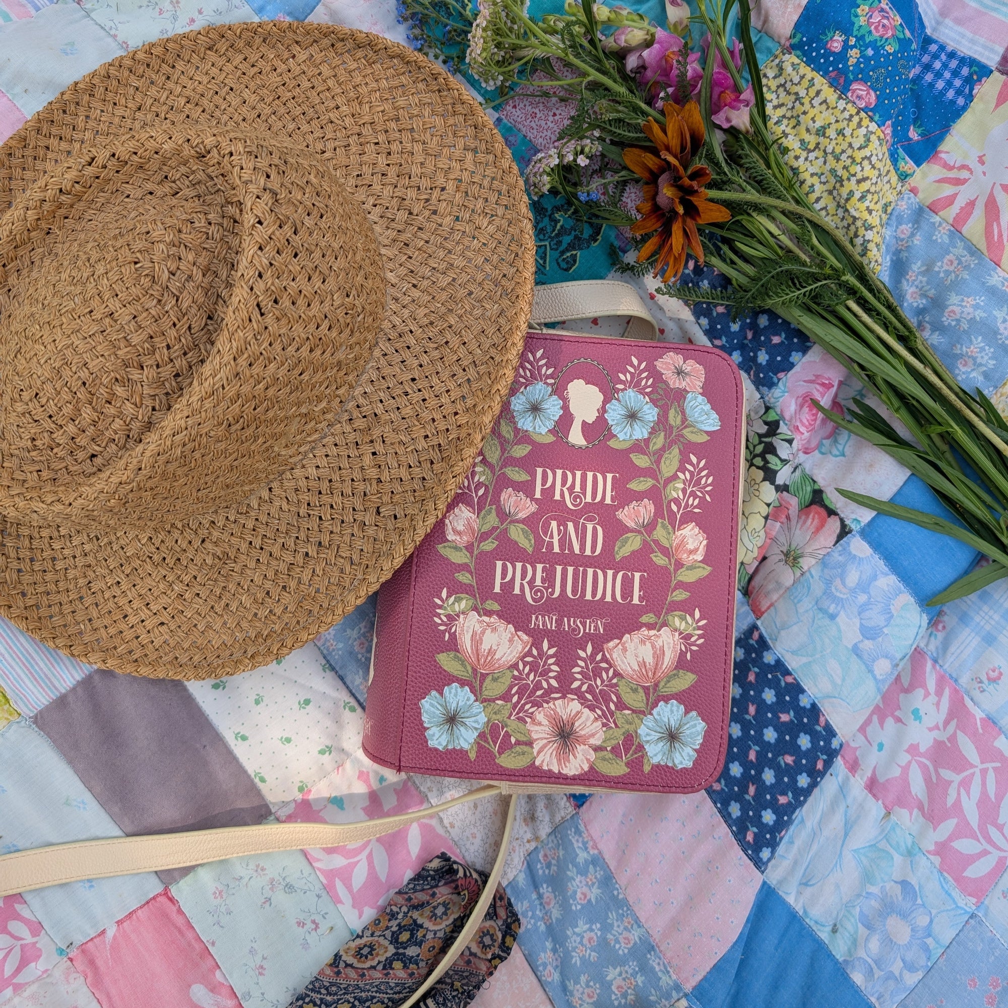Straw hat, book purse titled 'Pride and Prejudice', and flowers on a patchwork quilt