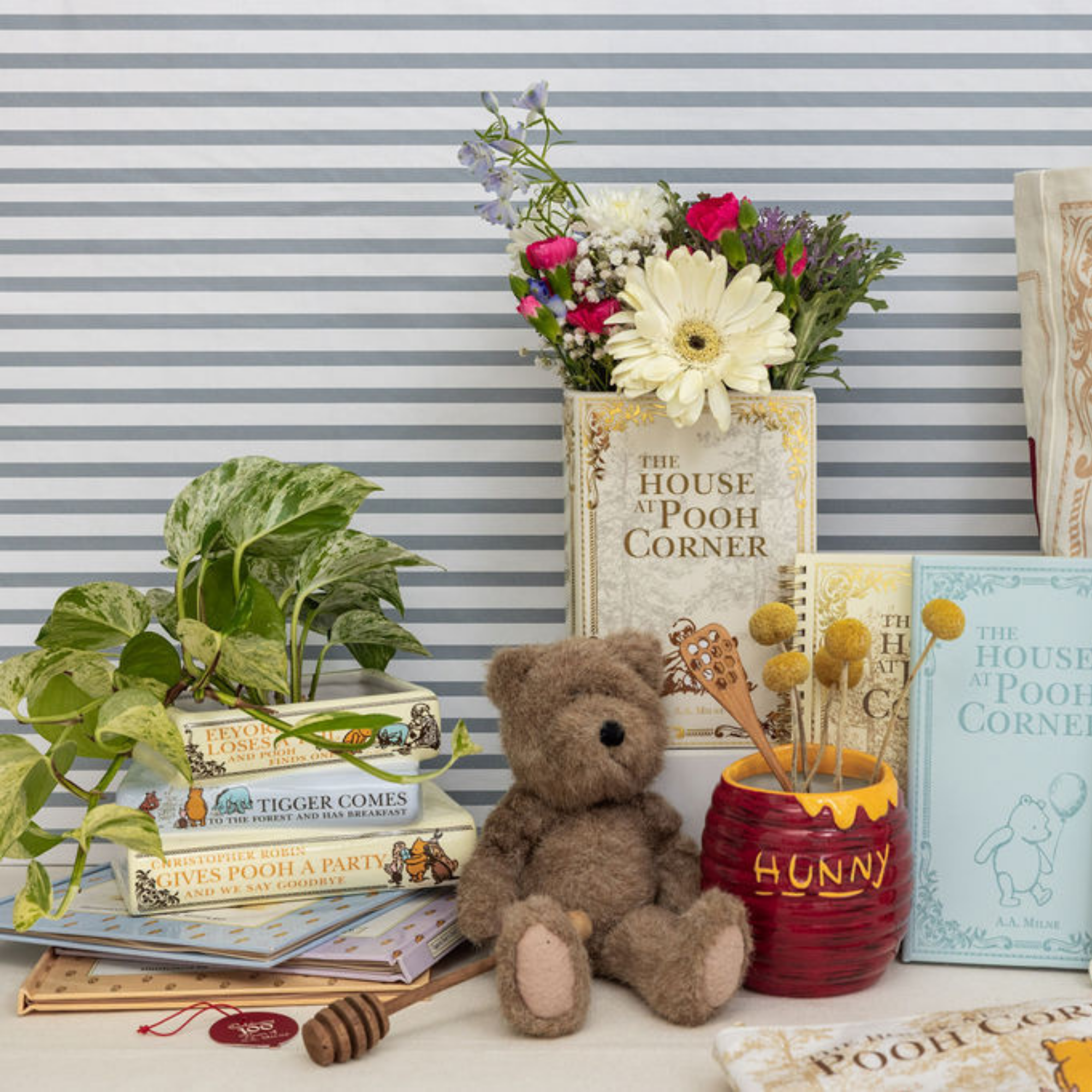 Teddy bear, books, and flowers on a striped wall background