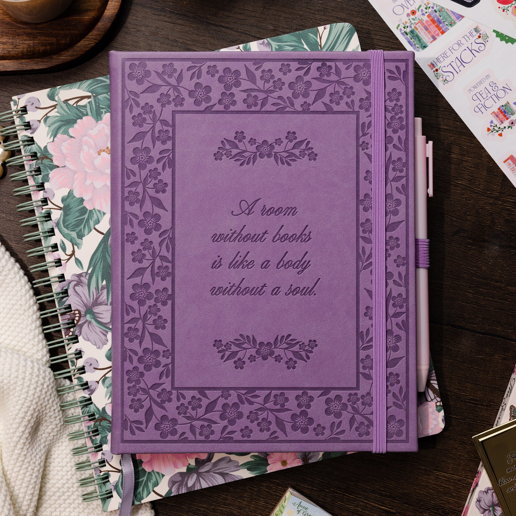 Purple notebook with floral design and text on a wooden surface with stationery items.