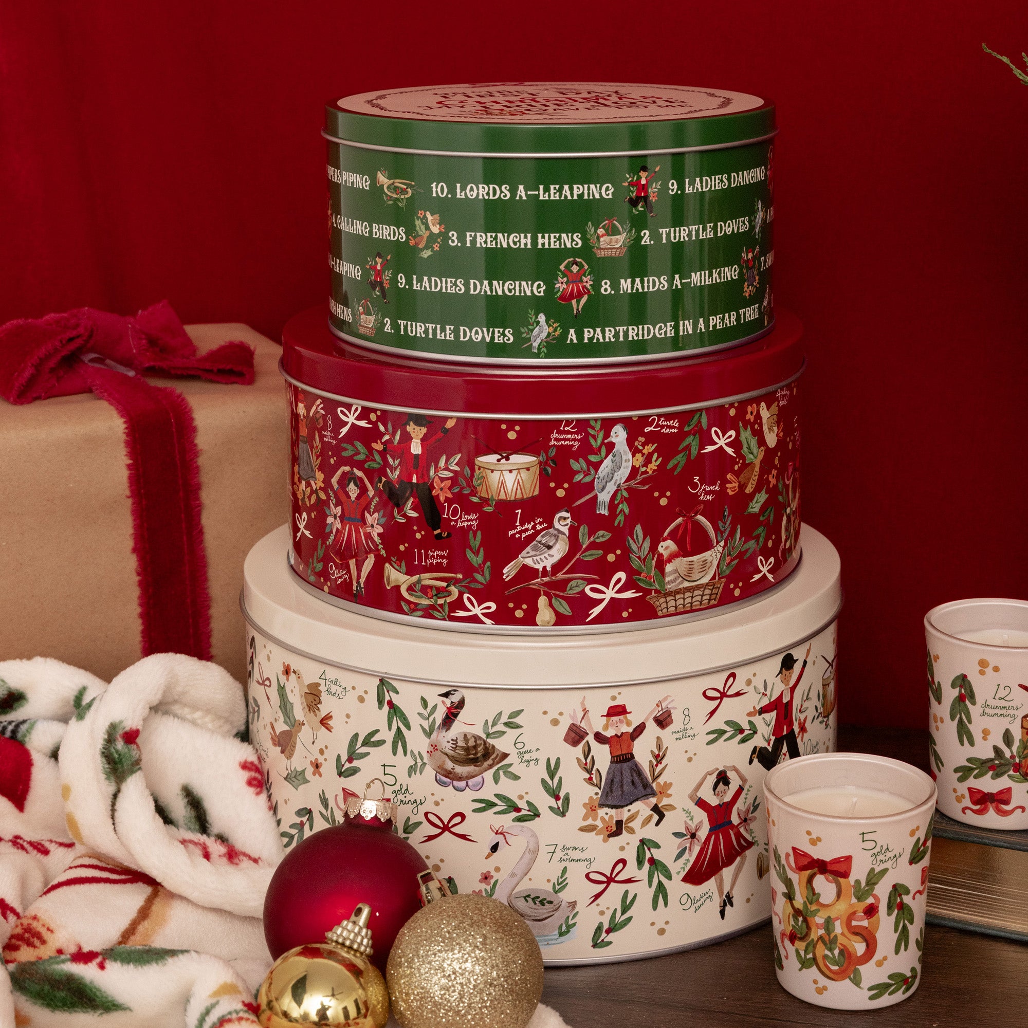 Three stacked round metal tins with Christmas-themed illustrations and text, photographed on a holiday themed background