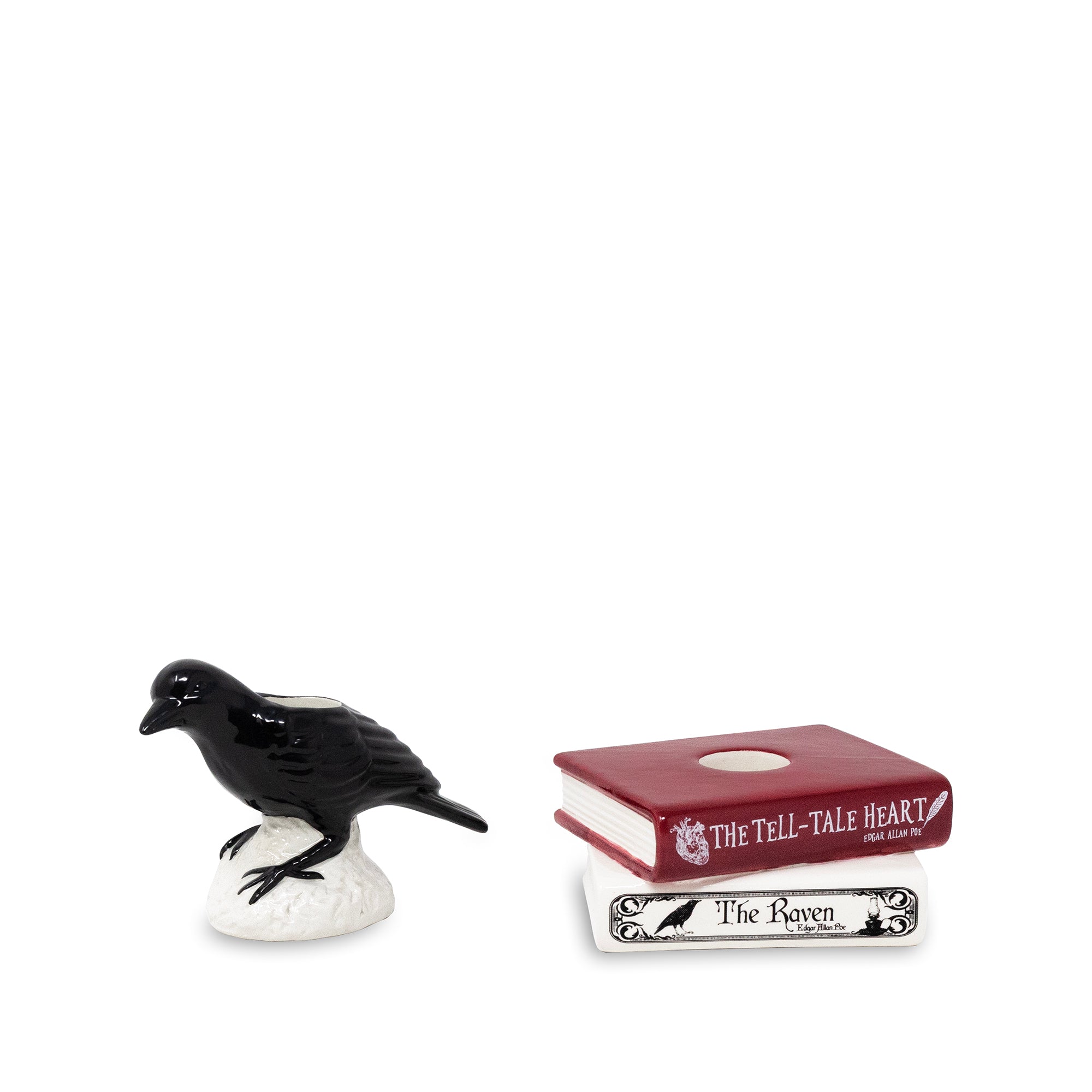 A small black raven figurine perched on a white base next to two miniature books from The Tell-Tale Heart: a dark red book labeled 'The Tell-Tale Heart' and a white book labeled 'The Raven'.