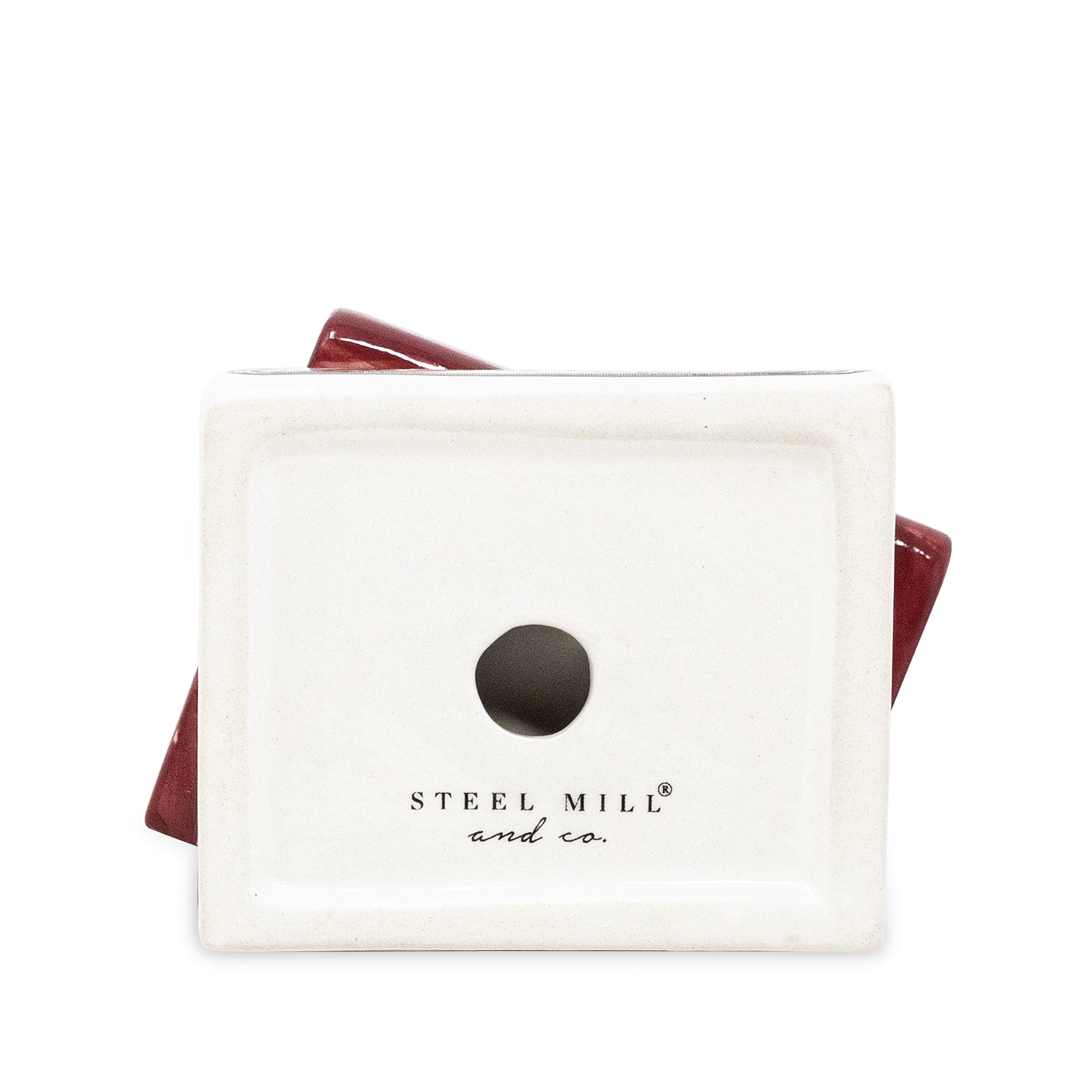 A square ceramic candleholder with a matte off-white face and a glossy dark red side edge, featuring a circular hole in the center and the text 'STEEL MILL and co.' printed below.