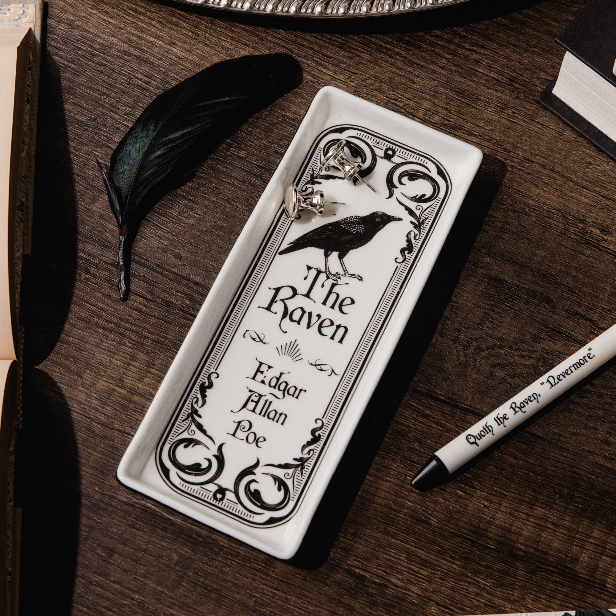 A white rectangular tray featuring a black ornate border, a raven illustration, and the text 'The Raven' and 'Edgar Allan Poe' printed in black on a brown background