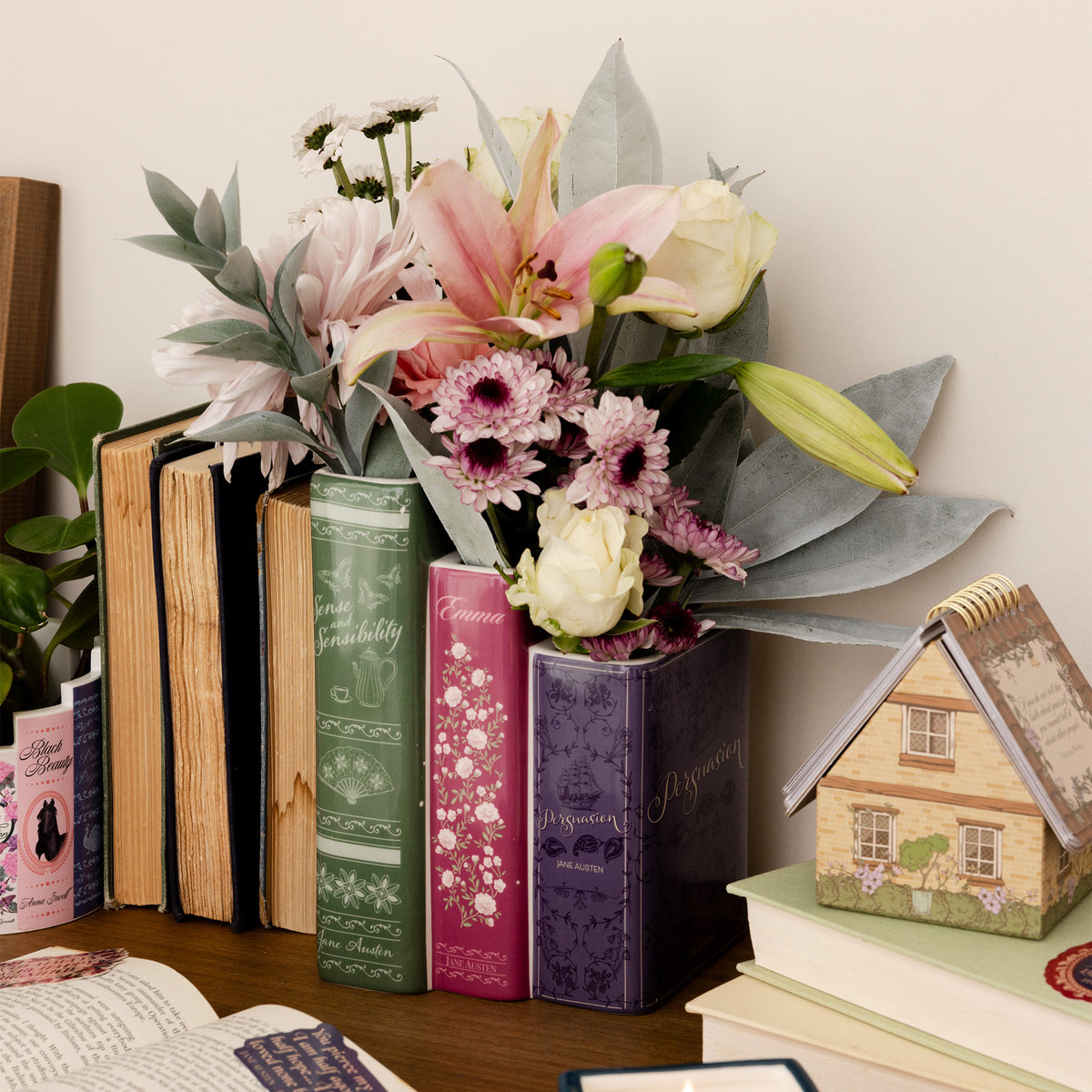 planter with three 'books' side by side. large green sense and sensibility, medium pink emma, and small purple persuasion with flowers inside on a desk