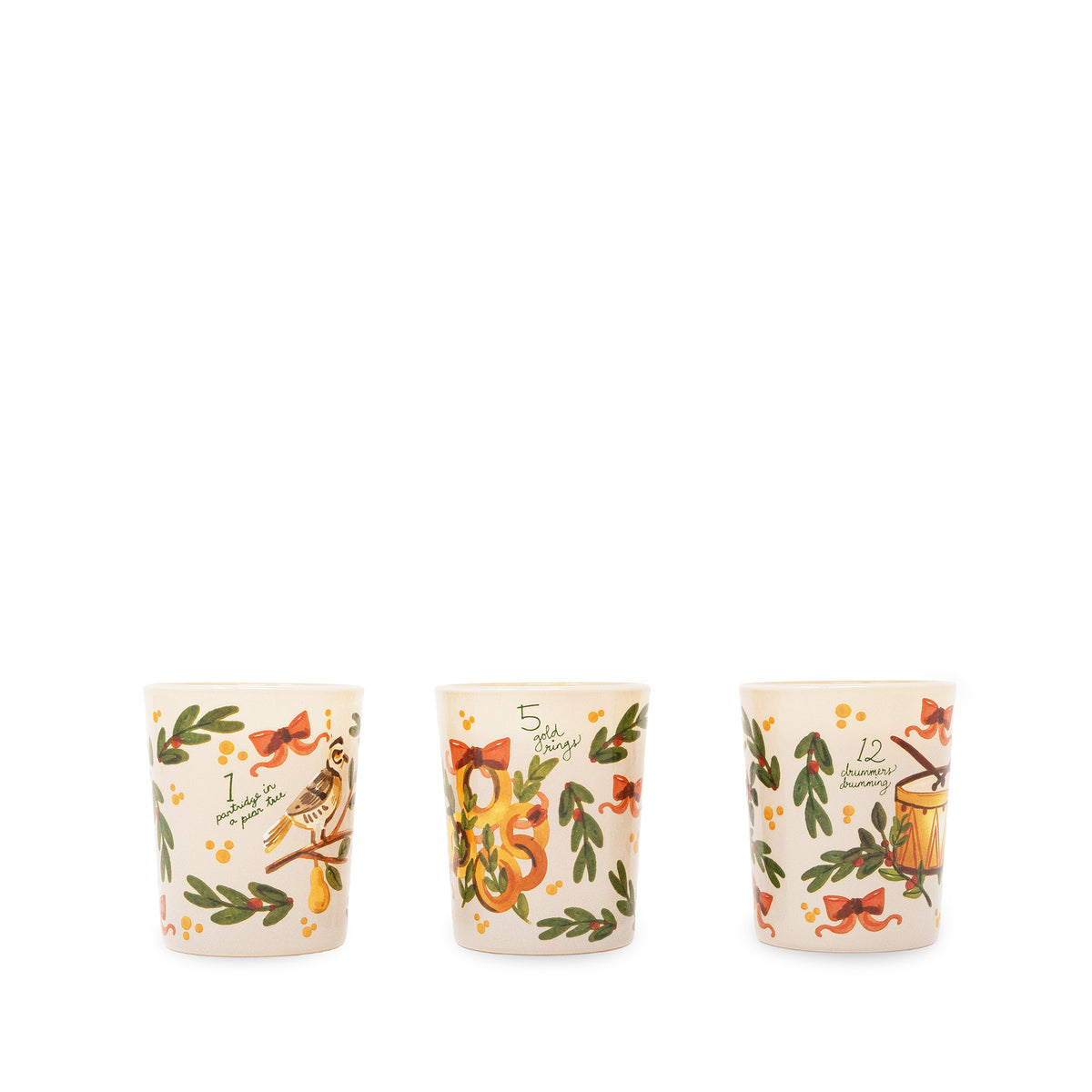 Three small ceramic candles with a warm cream background, decorated with green leaves, red bows, small yellow flowers, and illustrated holiday motifs including a bird, a nut, and a mug, shown on a plain white background.