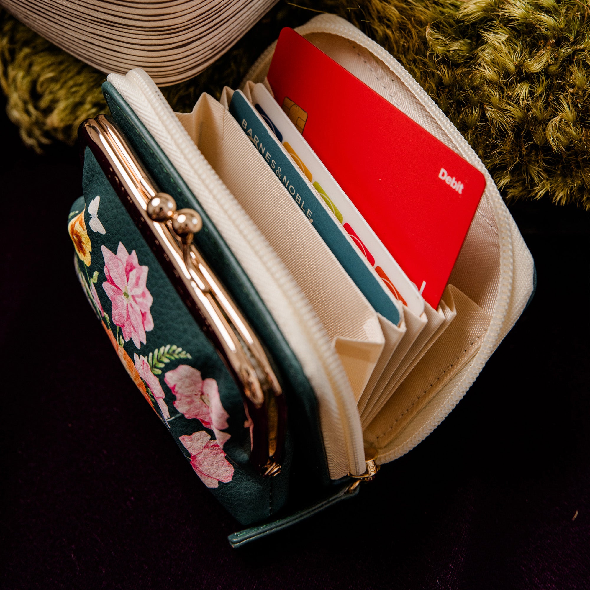 An open coin purse wallet, featuring a dark green exterior with a floral print on the front, cream-colored interior lining, gold-tone metal zipper and clasp, and multiple card slots.