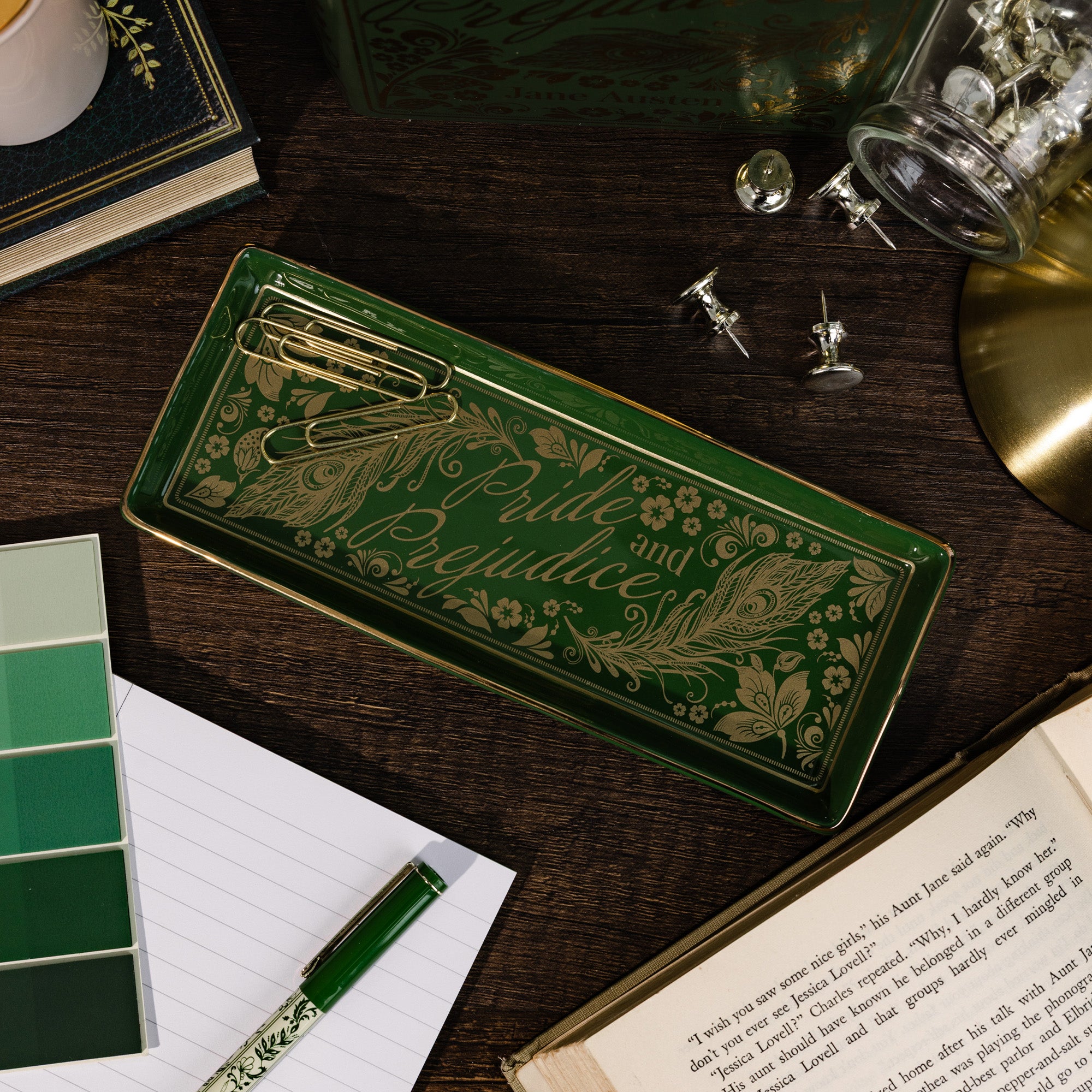 Decorative green tray with 'Pride and Prejudice' design on a wooden surface with books and stationery items.