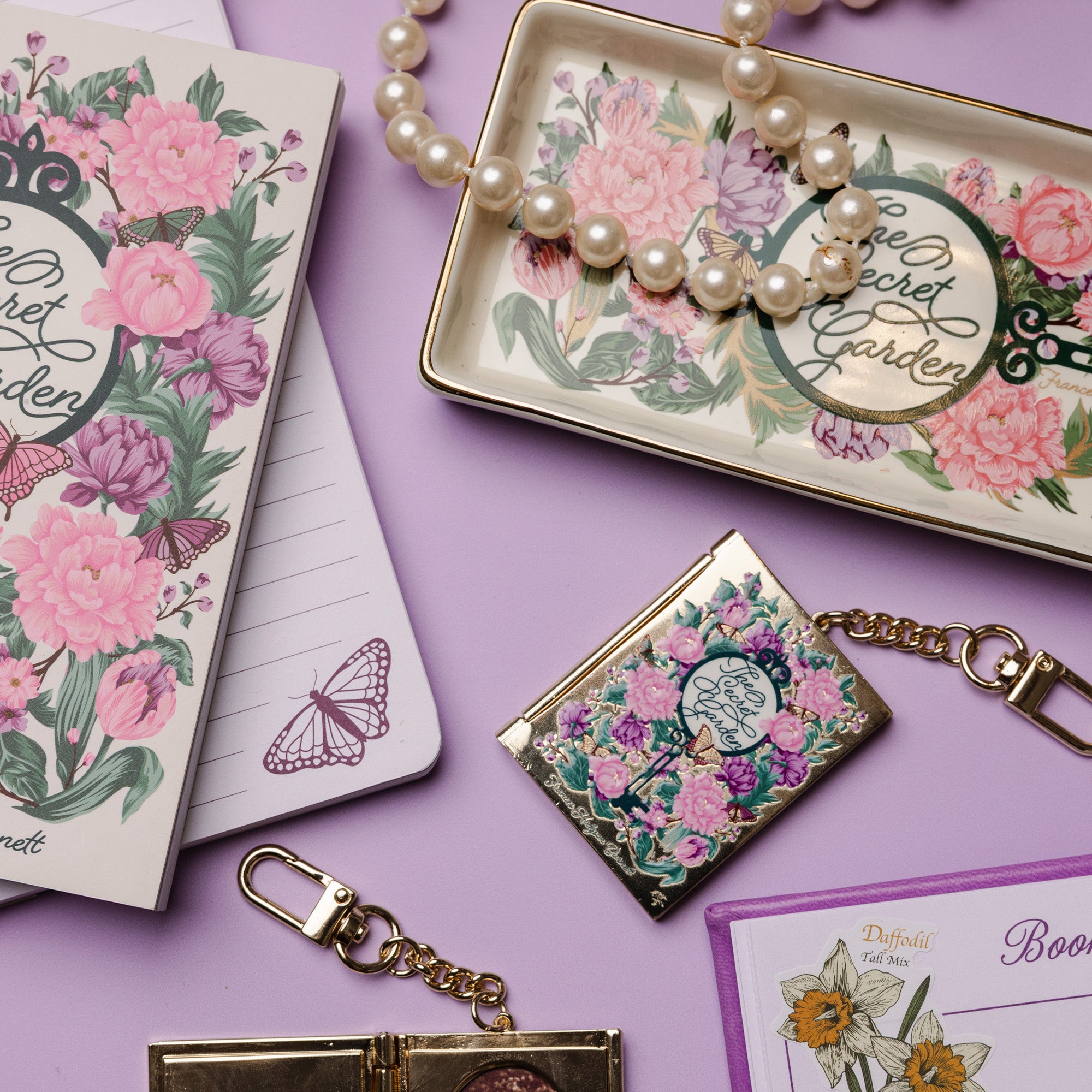 Floral-themed accessories including a notebook, keychain, and jewelry box on a purple background.