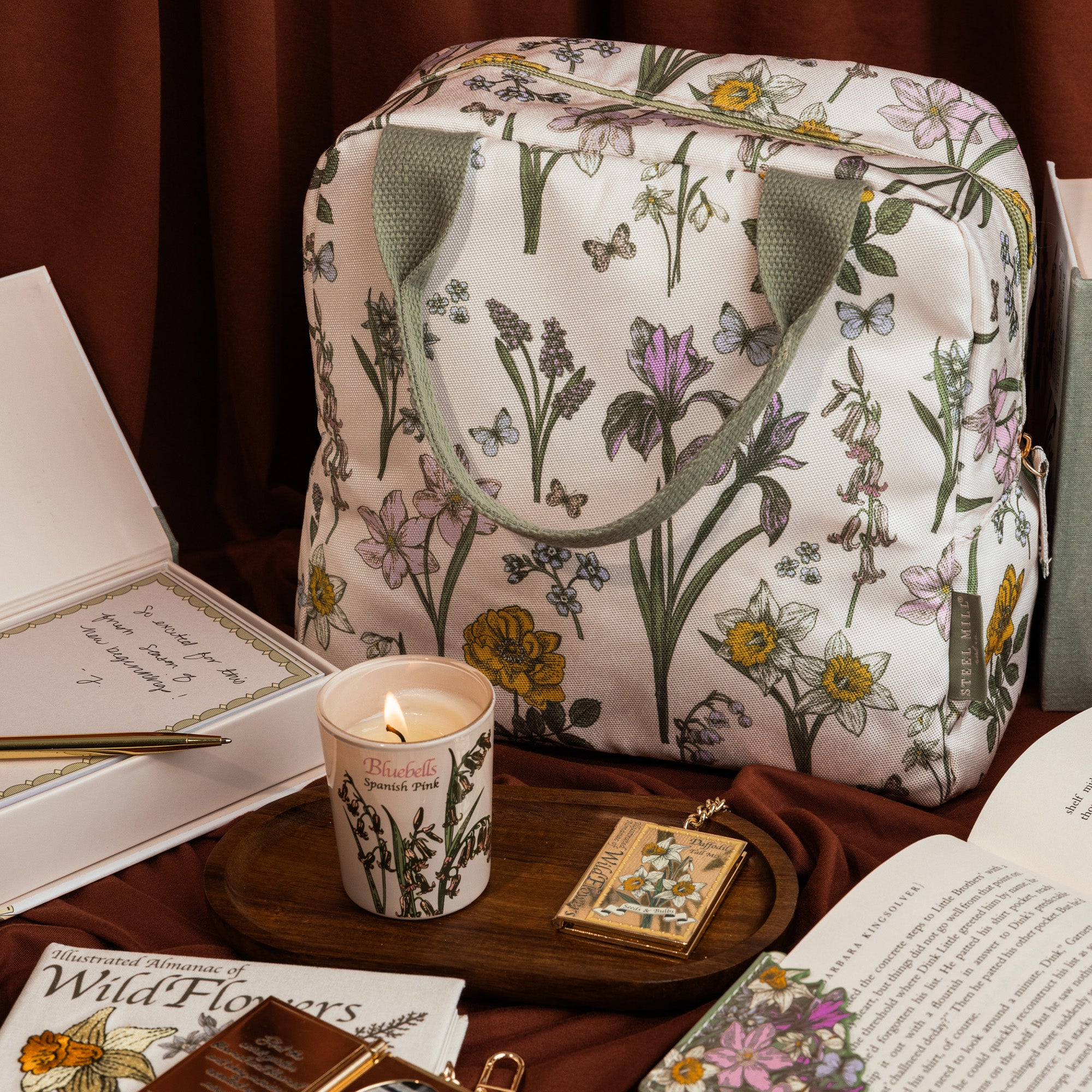 Floral-patterned lunch bag on a table with a lit candle and books
