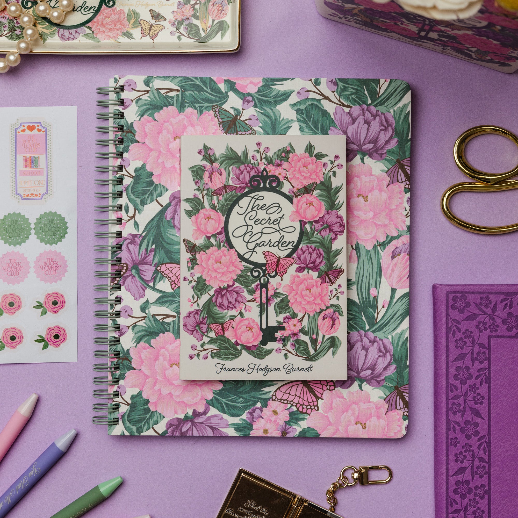 Floral notebook with decorative cover on a purple surface with stationery items.