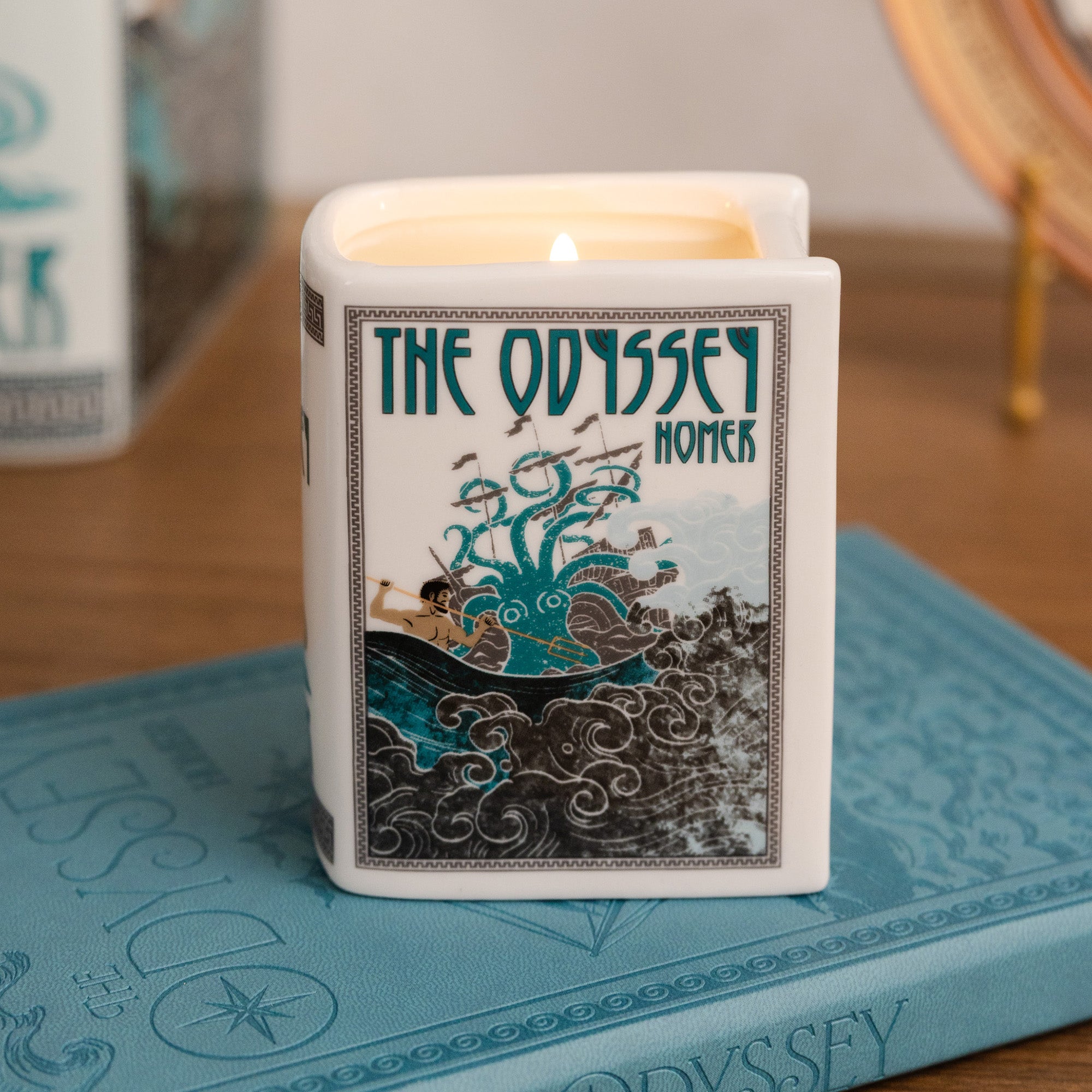 Candle in a container with 'The Odyssey' design on a book