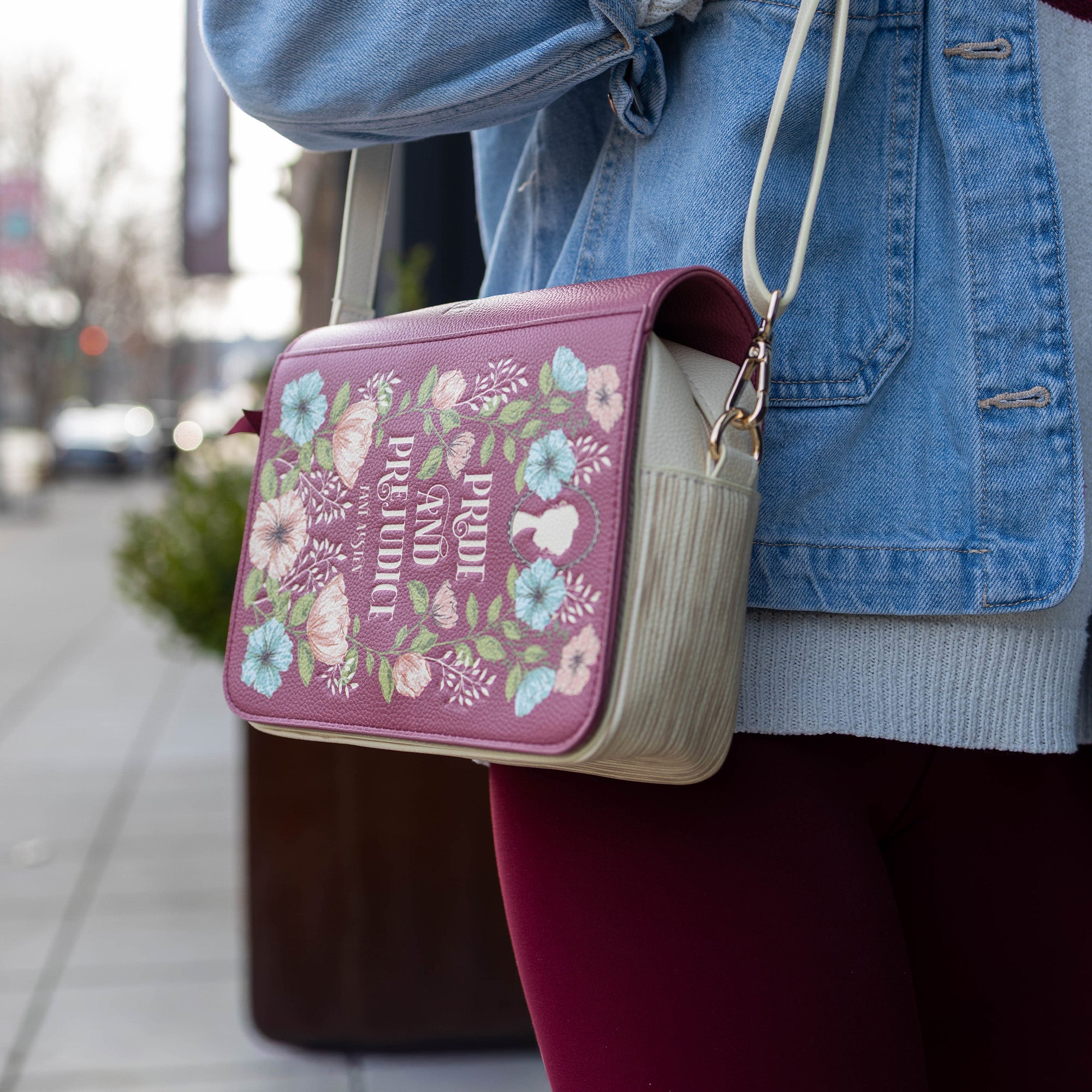 Person holding a pink crossbody bag with floral design and text.