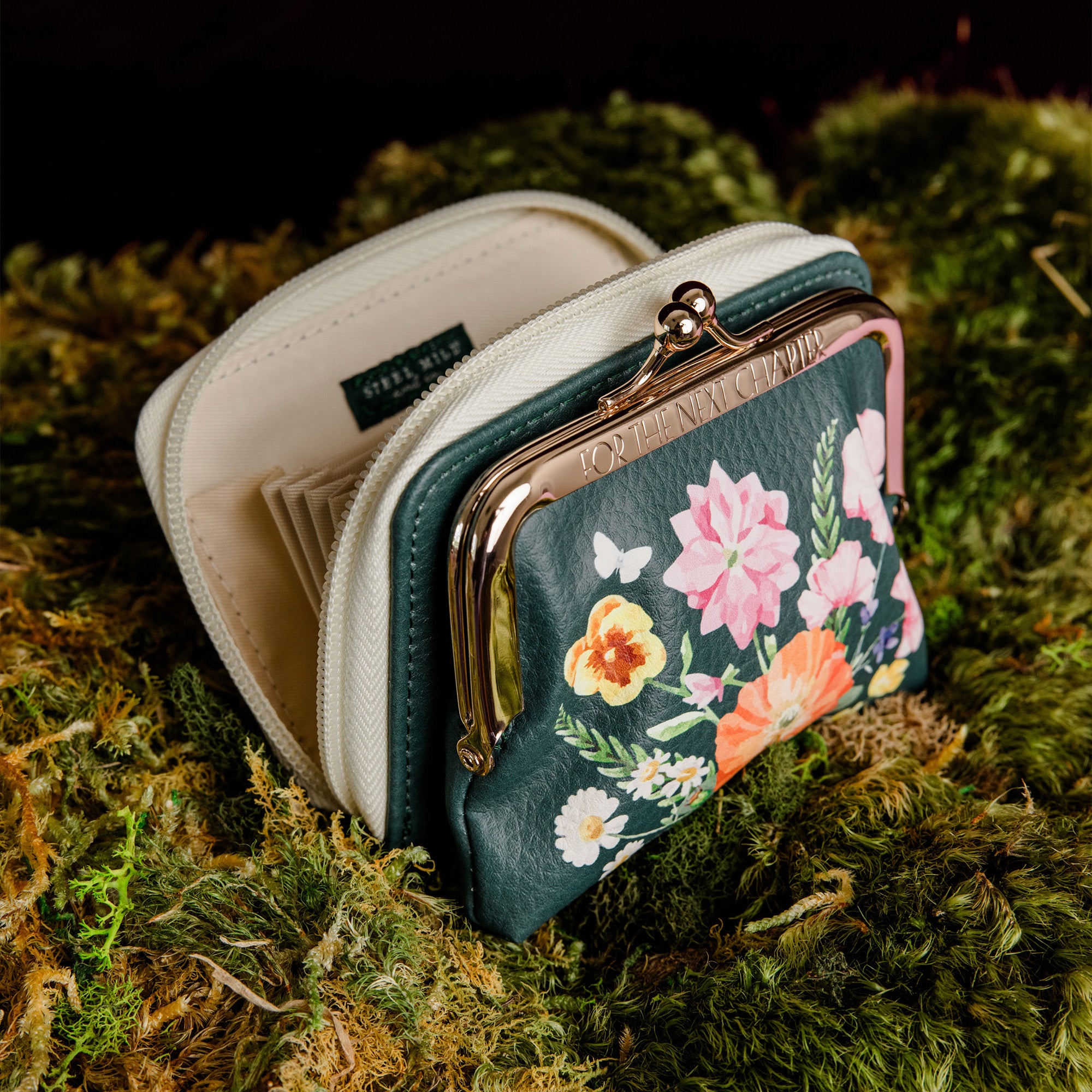 opened A small kiss-lock coin purse with a cream-colored frame and zipper, featuring a dark green front panel decorated with a colorful floral print of pink, orange, yellow, and white flowers on a purple base and black ground